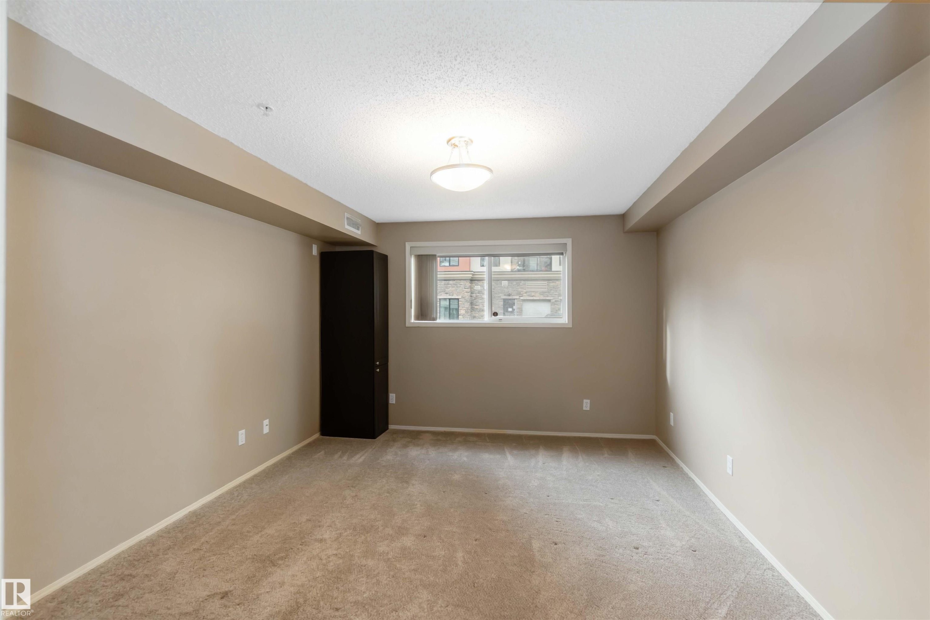 Unfurnished room featuring light carpet and a textured ceiling - 113 10311 111 Street, Edmonton, AB - Indoor Photo Showing Other Room
