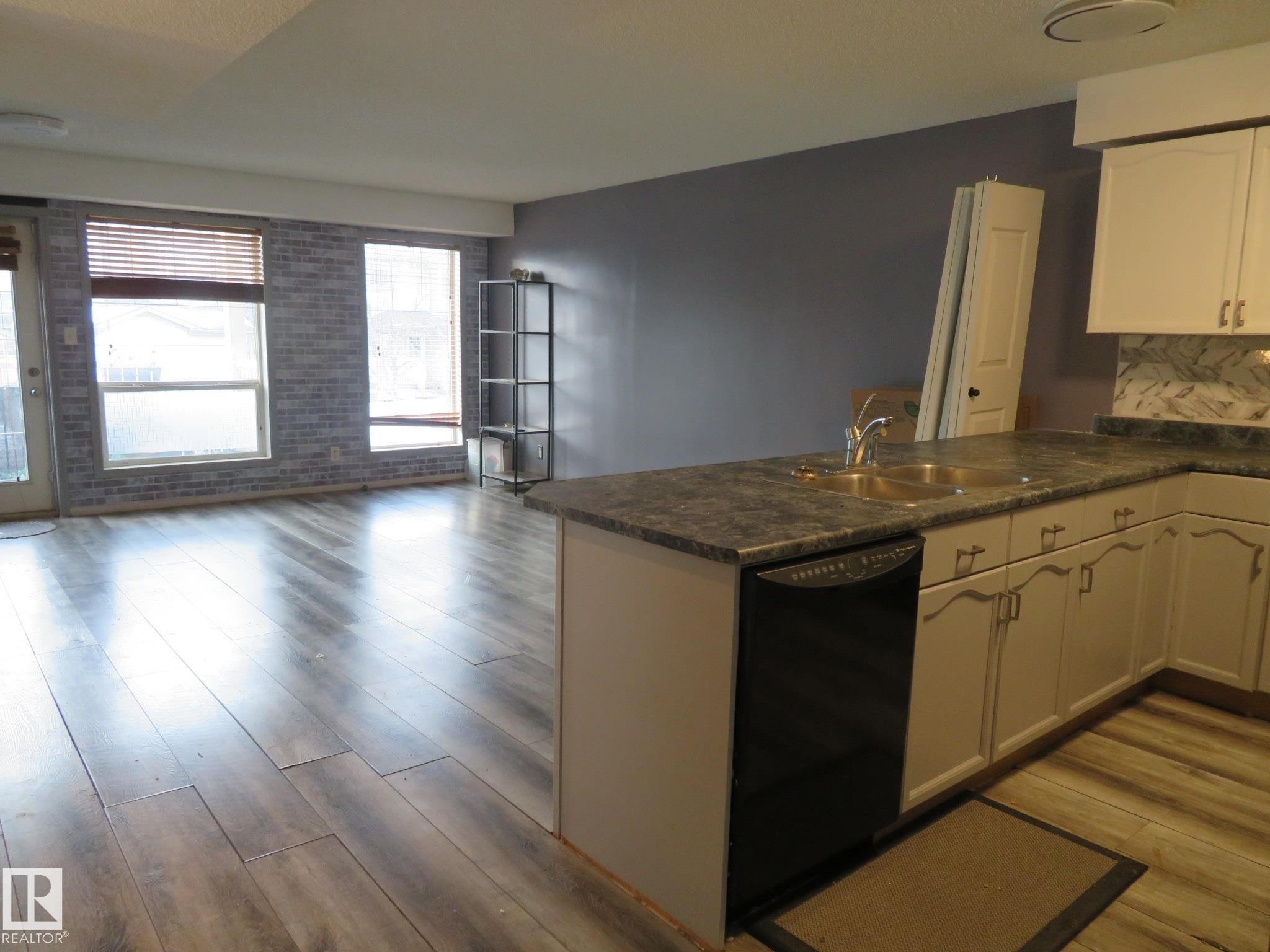 Kitchen with a peninsula, dark countertops, white cabinets, black dishwasher, and brick wall - 2945 26 Street, Edmonton, AB - Indoor Photo Showing Kitchen
