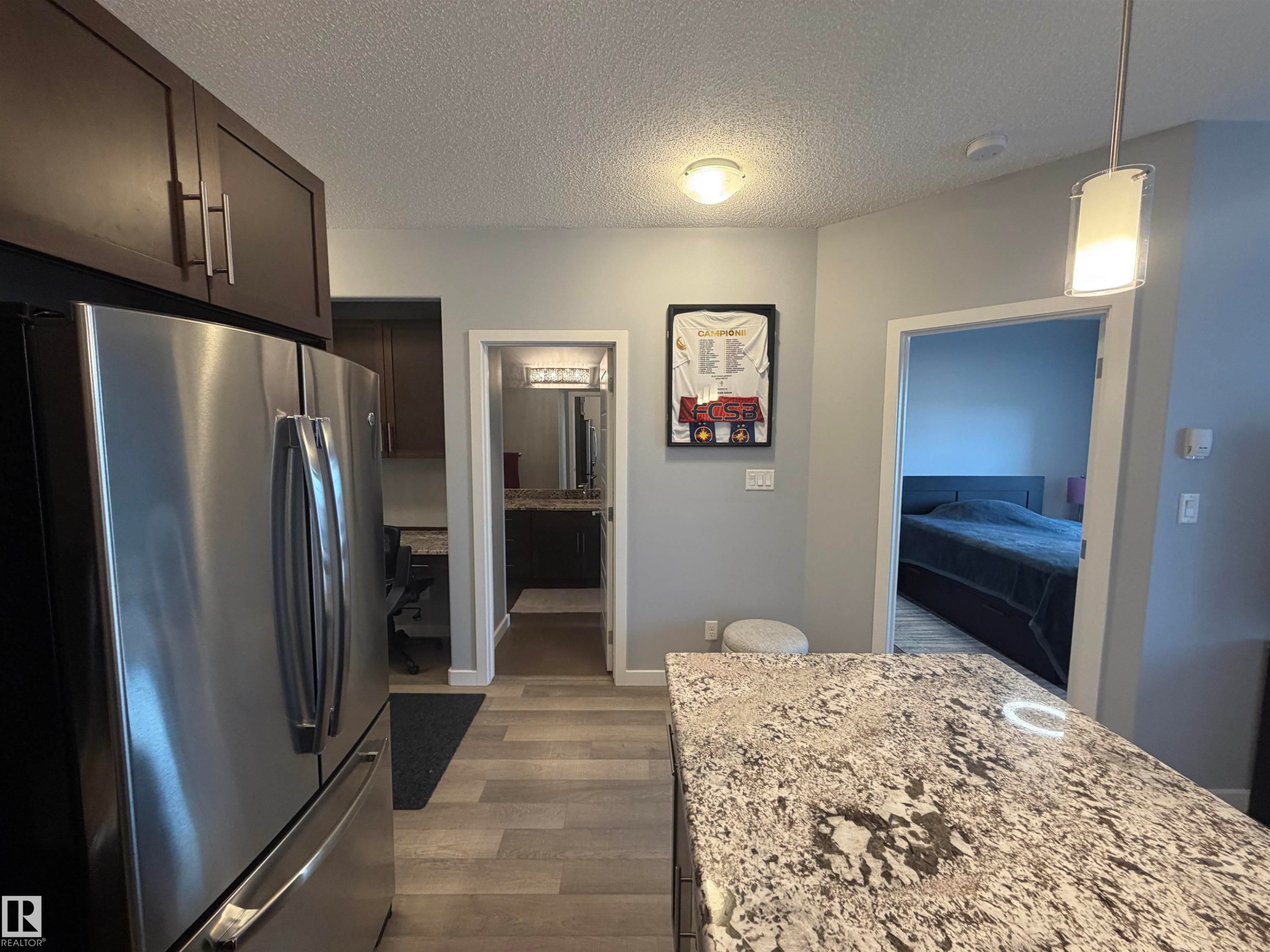 Kitchen featuring freestanding refrigerator, a textured ceiling, dark wood-style floors, pendant lighting, and light stone countertops - 417 1004 Rosenthal Boulevard, Edmonton, AB - Indoor Photo Showing Kitchen