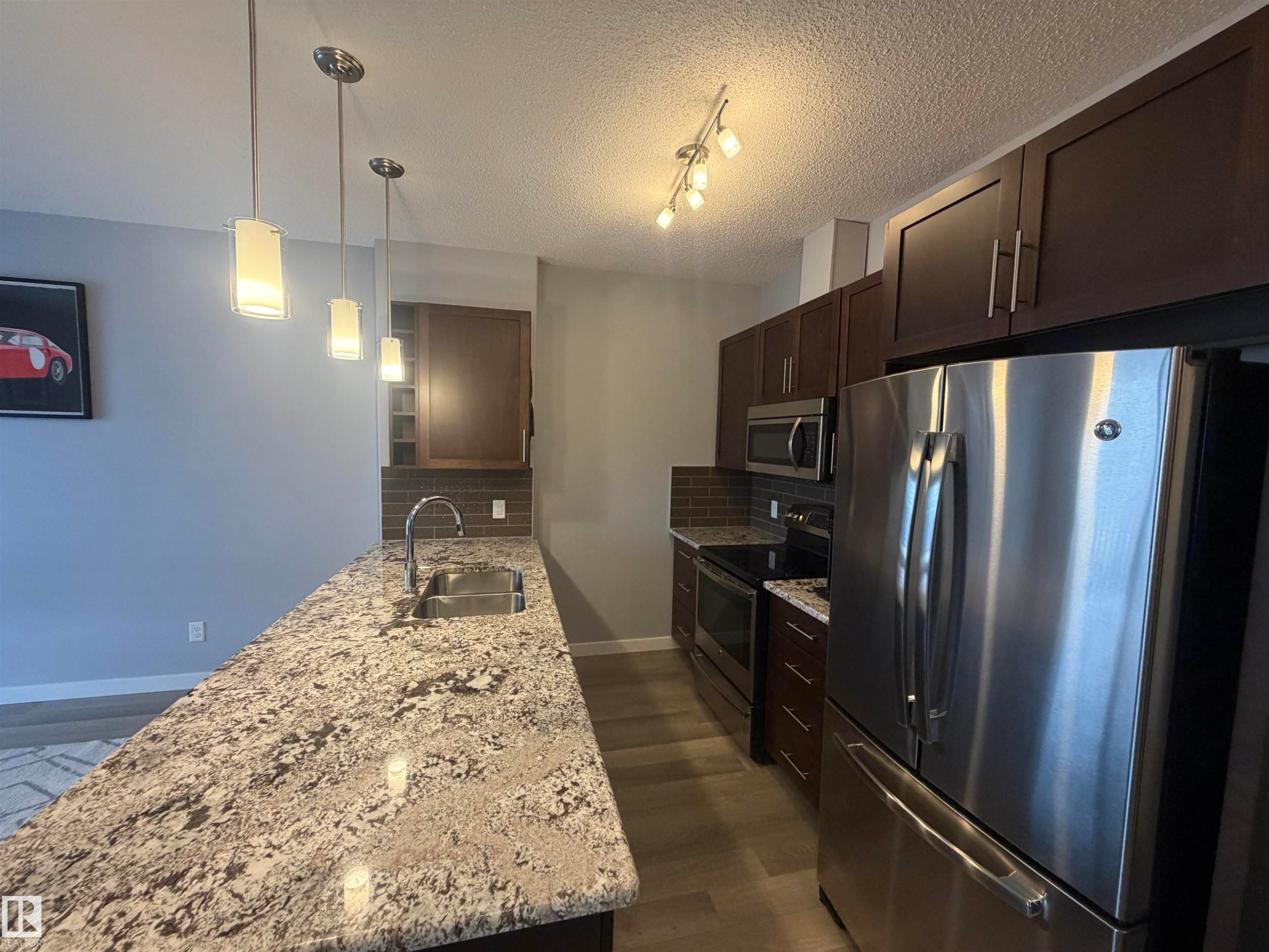 Kitchen featuring stainless steel appliances, a peninsula, decorative backsplash, light stone countertops, and a textured ceiling - 417 1004 Rosenthal Boulevard, Edmonton, AB - Indoor Photo Showing Kitchen With Stainless Steel Kitchen With Double Sink