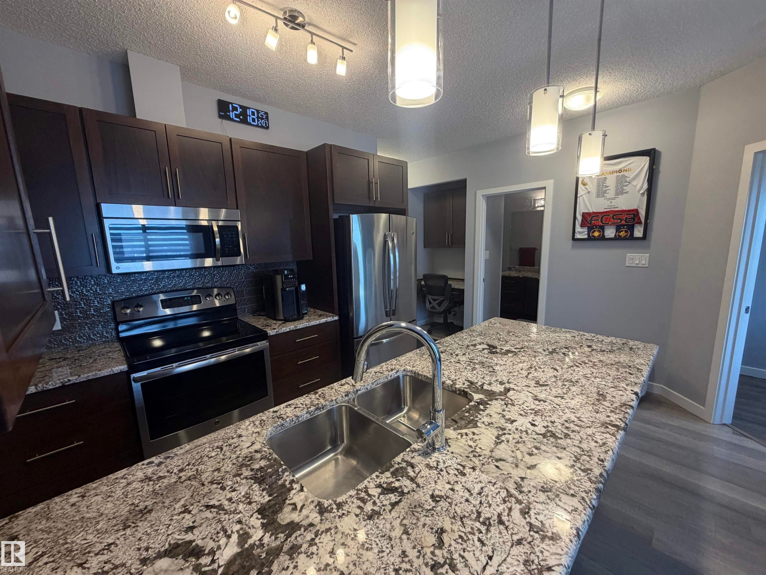 Kitchen with dark wood finish cabinets, stainless steel appliances, hanging light fixtures, dark wood-style flooring, and a textured ceiling - 417 1004 Rosenthal Boulevard, Edmonton, AB - Indoor Photo Showing Kitchen With Stainless Steel Kitchen With Double Sink With Upgraded Kitchen