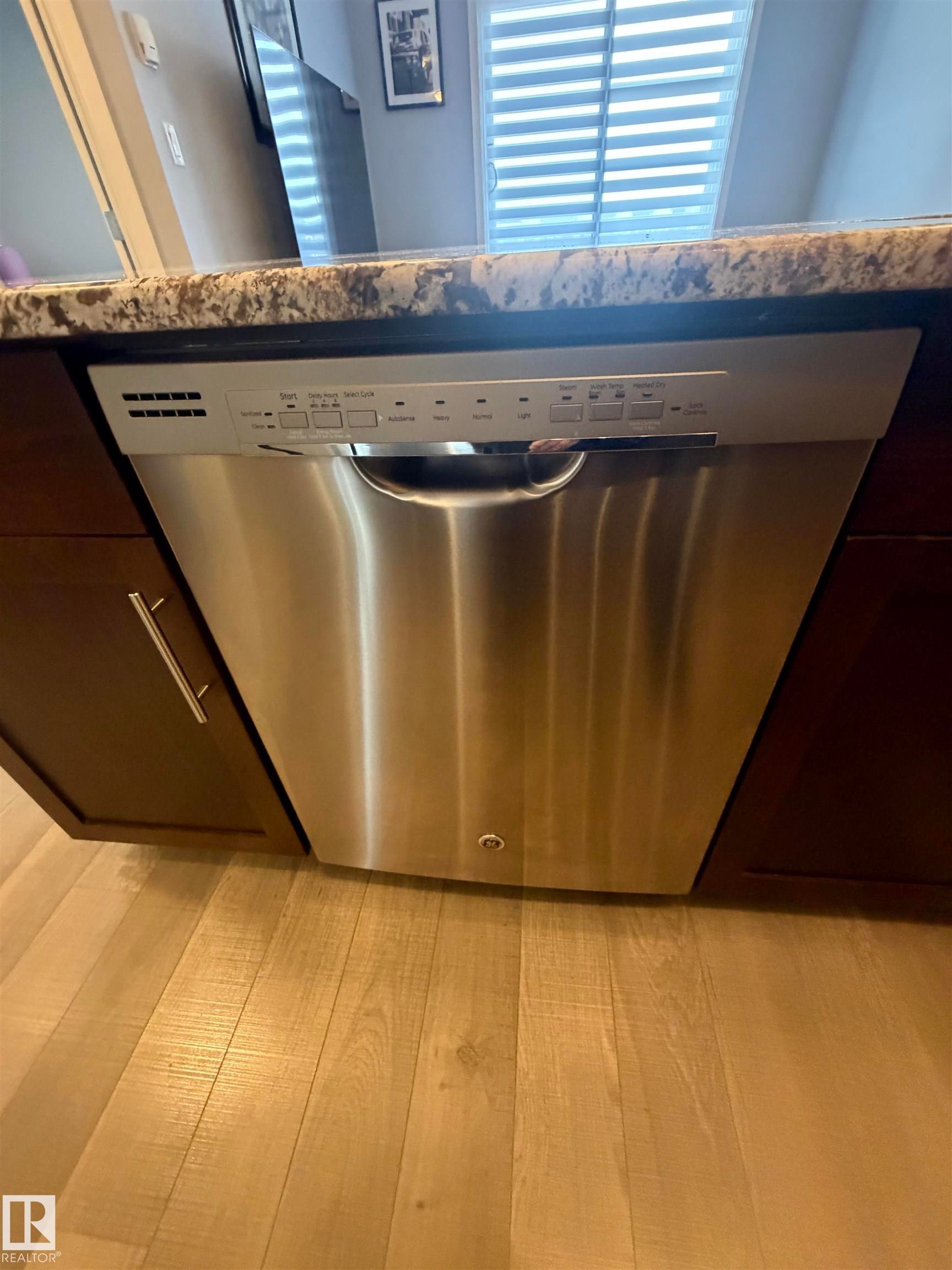 Kitchen view of stainless steel dishwasher, light wood-style floors, and stone counters - 417 1004 Rosenthal Boulevard, Edmonton, AB - Indoor