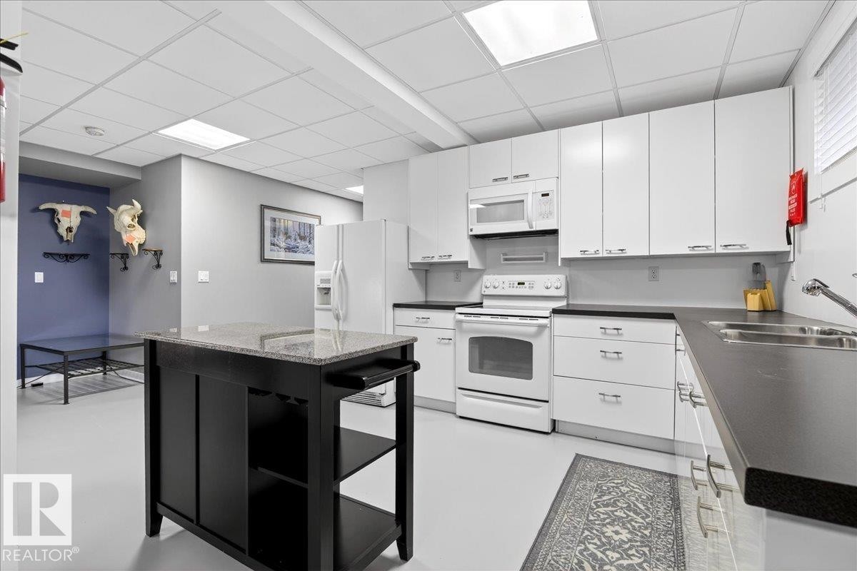 Kitchen with white appliances, a paneled ceiling, white cabinets, a kitchen island, and concrete flooring - 5019 48 Avenue, Chipman, AB - Indoor Photo Showing Kitchen