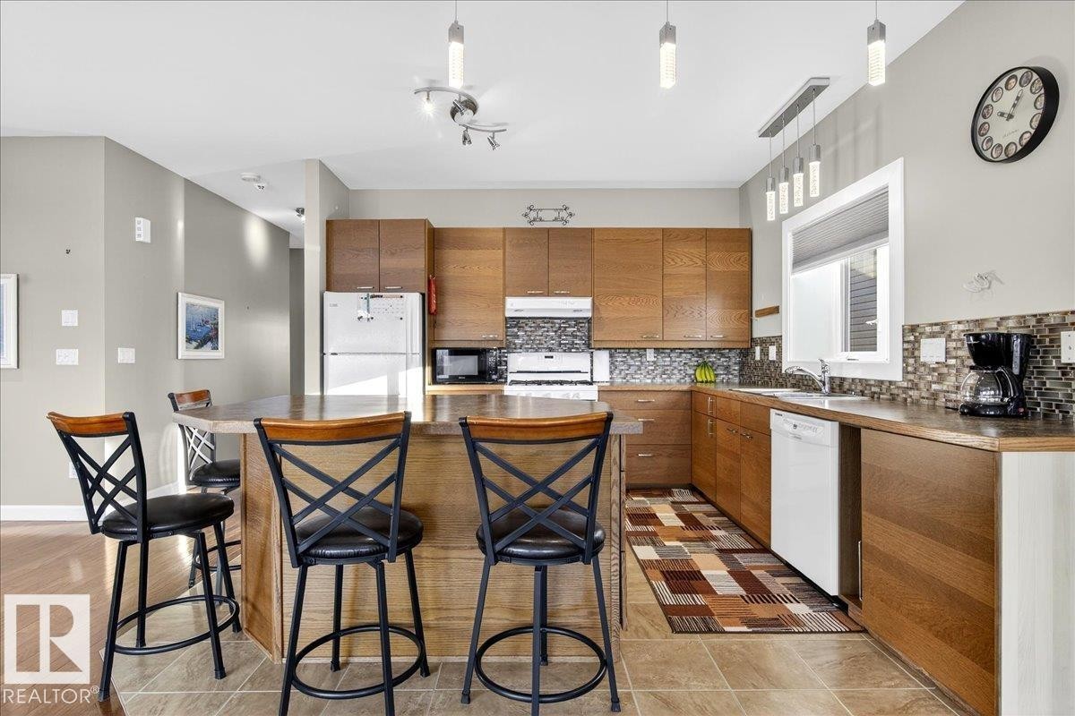 Kitchen featuring wood finish cabinetry, a kitchen bar, decorative light fixtures, backsplash, and a center island - 5019 48 Avenue, Chipman, AB - Indoor Photo Showing Kitchen