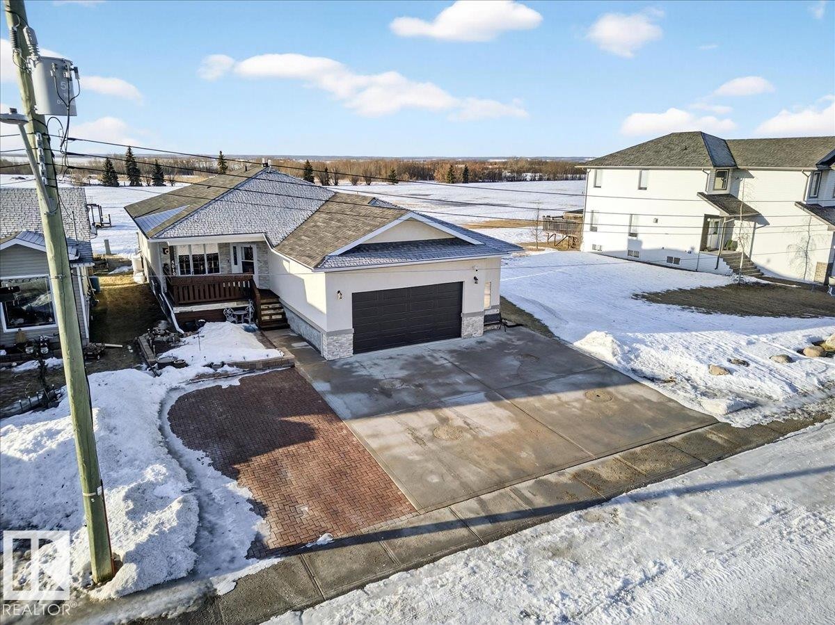 View of front of house featuring stone siding, driveway, an attached garage, a wooden deck, and stucco siding - 5019 48 Avenue, Chipman, AB - Outdoor