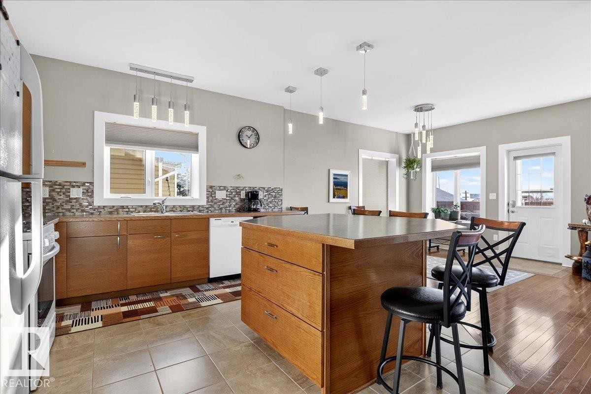 Kitchen featuring a breakfast bar area, tasteful backsplash, wood finish cabinetry, white appliances, and pendant lighting - 5019 48 Avenue, Chipman, AB - Indoor Photo Showing Kitchen