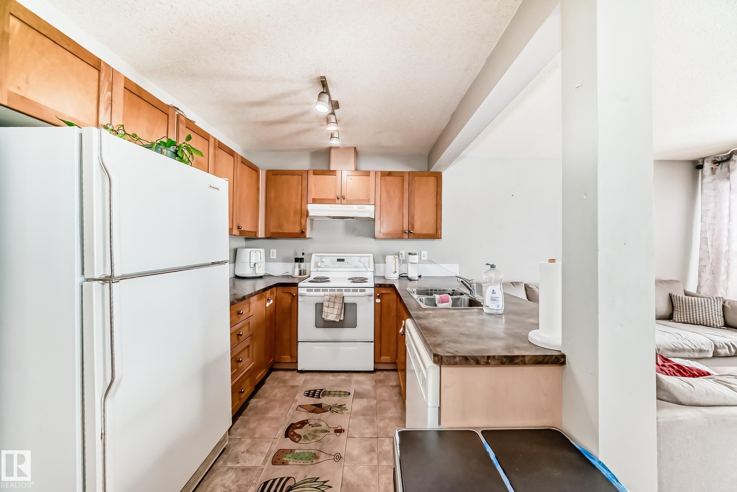 Kitchen with white appliances, a textured ceiling, dark countertops, wood finish cabinets, and a peninsula - 185 230 Edwards Drive, Edmonton, AB