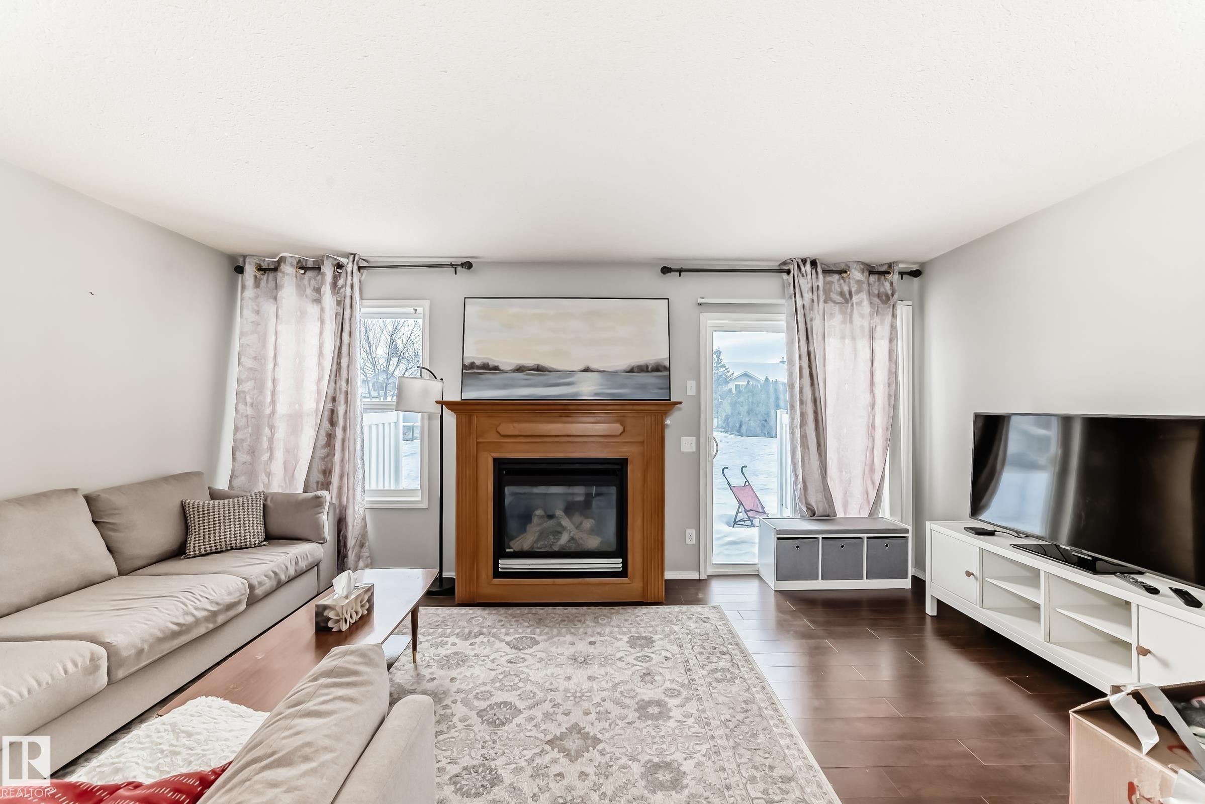 Living area with a glass covered fireplace, dark wood-type flooring, and plenty of natural light - 185 230 Edwards Drive, Edmonton, AB