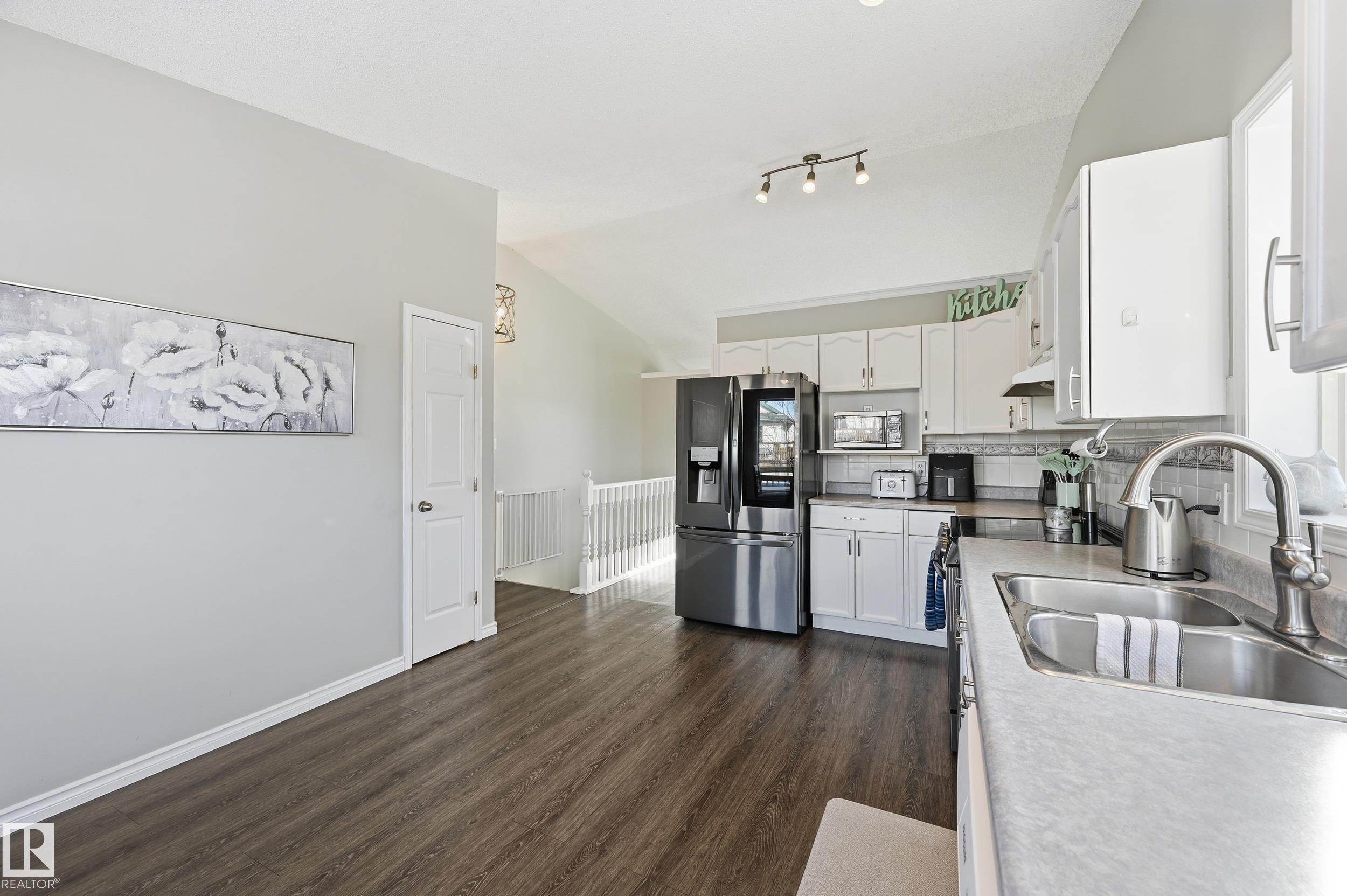 Kitchen with lofted ceiling, white cabinetry, stainless steel appliances, dark wood-style floors, and decorative backsplash - 2952 39 Avenue, Edmonton, AB - Indoor Photo Showing Kitchen With Double Sink