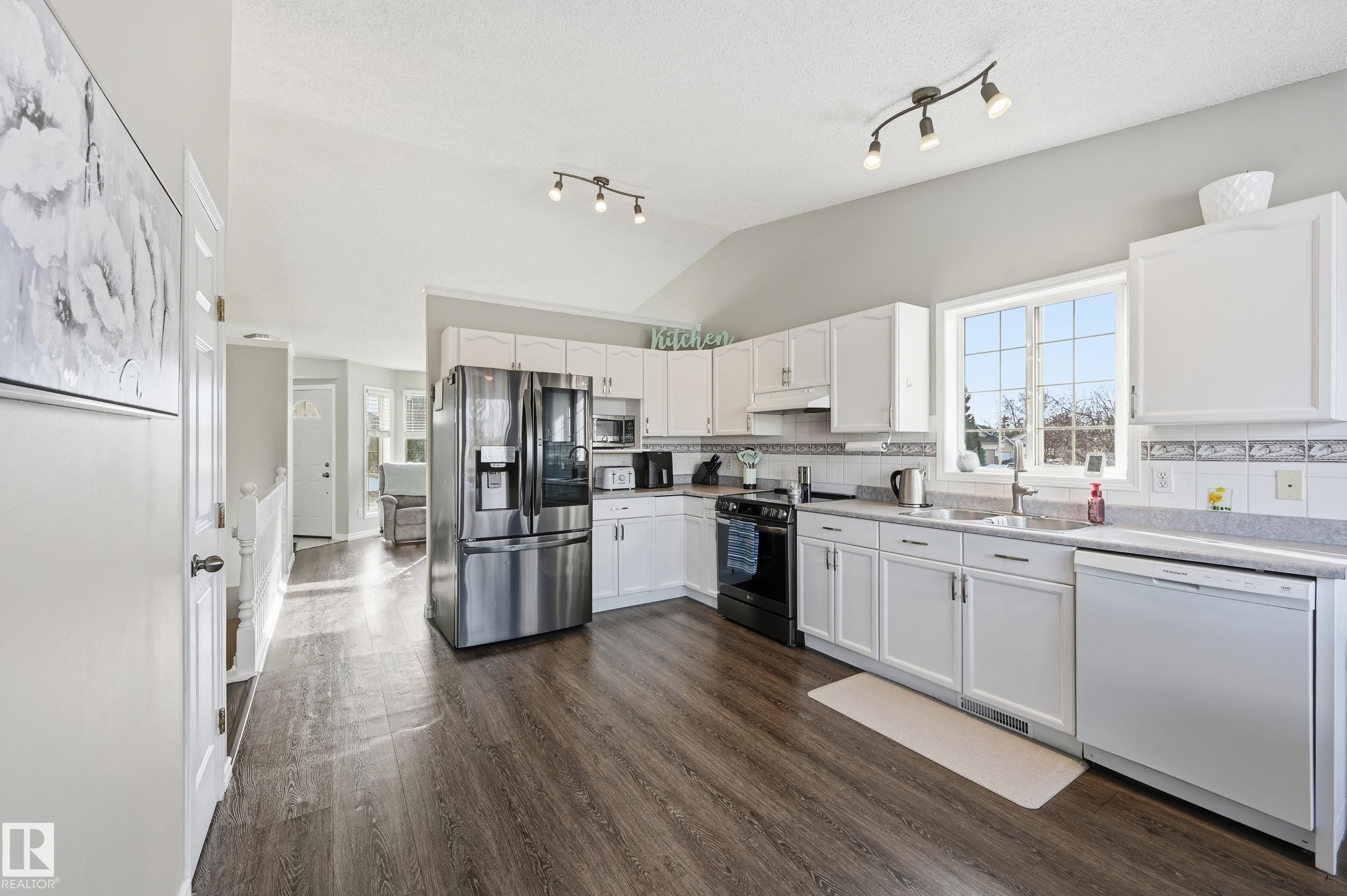 Kitchen with stainless steel appliances, white cabinetry, dark wood-type flooring, backsplash, and lofted ceiling - 2952 39 Avenue, Edmonton, AB - Indoor Photo Showing Kitchen