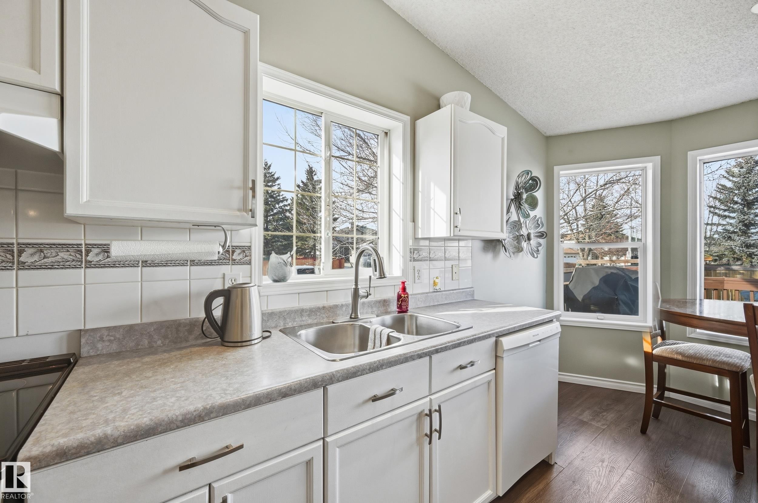 Kitchen with white cabinets, tasteful backsplash, dishwasher, dark wood-style flooring, and light countertops - 2952 39 Avenue, Edmonton, AB - Indoor Photo Showing Kitchen With Double Sink