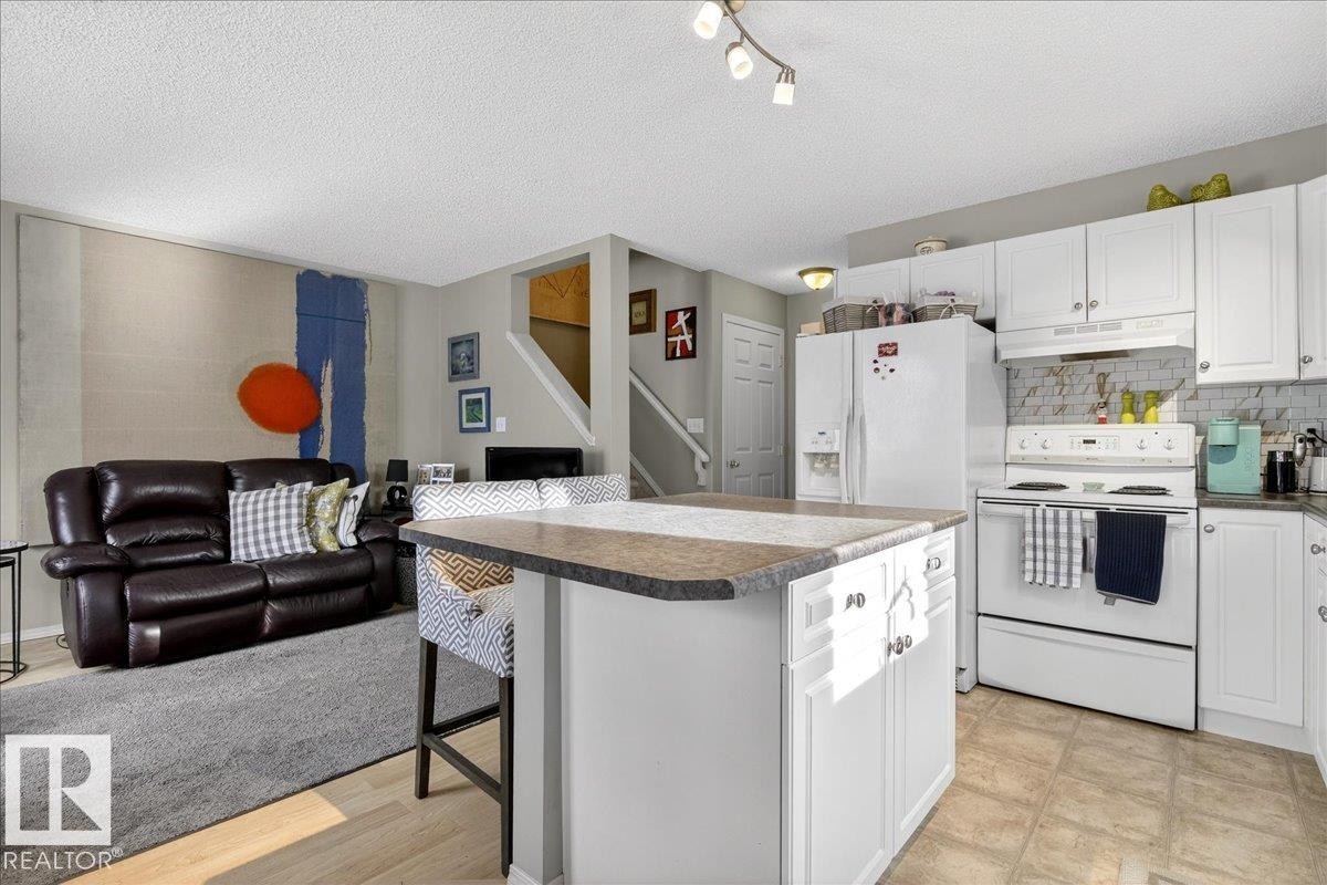 Kitchen featuring a kitchen breakfast bar, white appliances, open floor plan, white cabinetry, and a textured ceiling - 23 4020 21 Street, Edmonton, AB - Indoor Photo Showing Kitchen