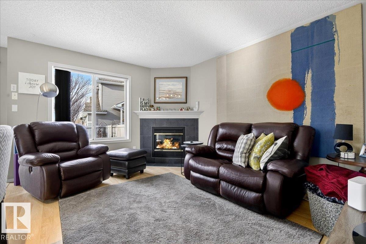 Living room with wood finished floors, a textured ceiling, and a tiled fireplace - 23 4020 21 Street, Edmonton, AB - Indoor Photo Showing Living Room With Fireplace