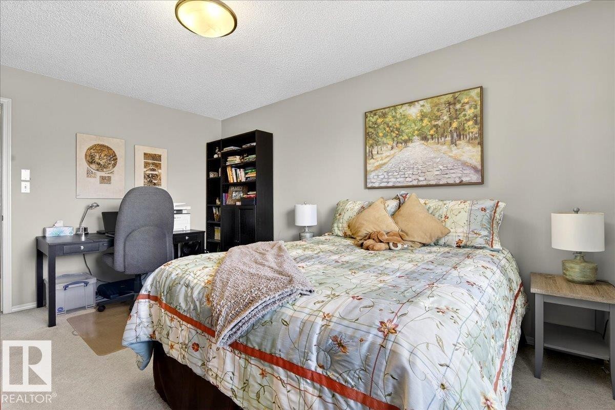 Carpeted bedroom with a textured ceiling and an office area - 23 4020 21 Street, Edmonton, AB - Indoor Photo Showing Bedroom