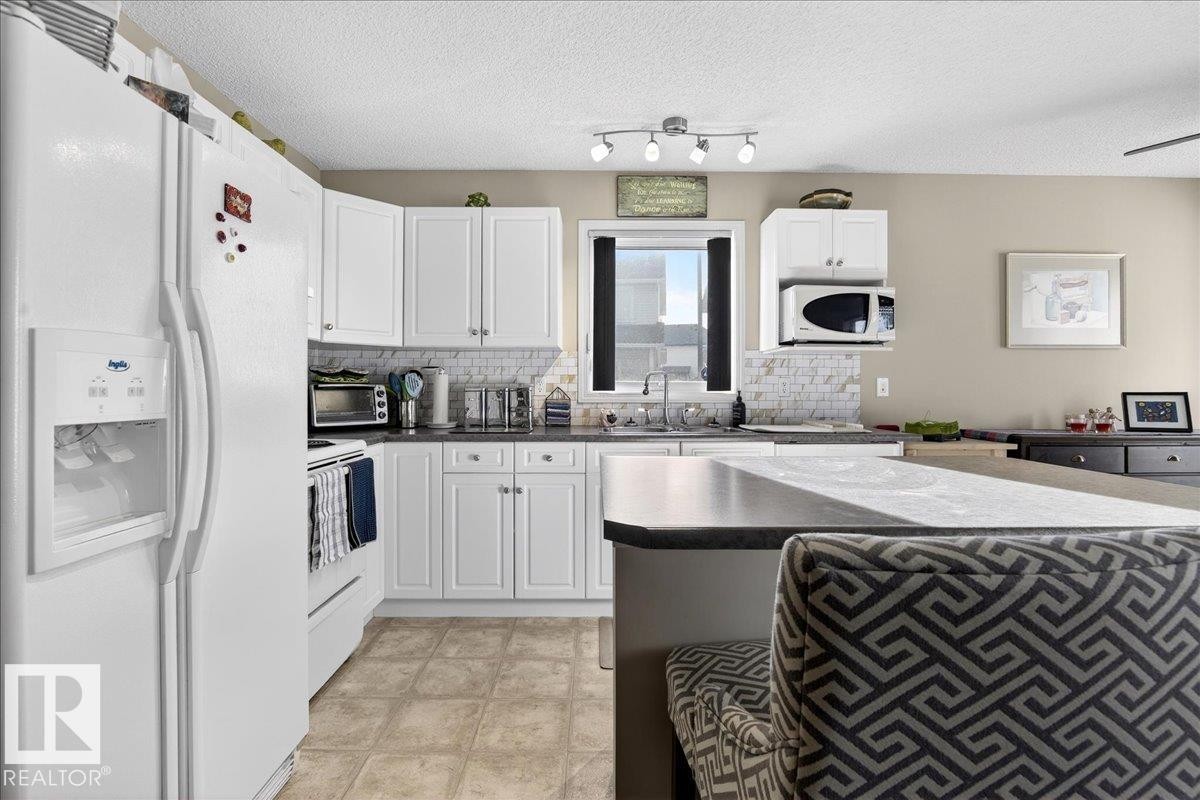 Kitchen with dark countertops, white appliances, white cabinets, tasteful backsplash, and a textured ceiling - 23 4020 21 Street, Edmonton, AB - Indoor Photo Showing Kitchen