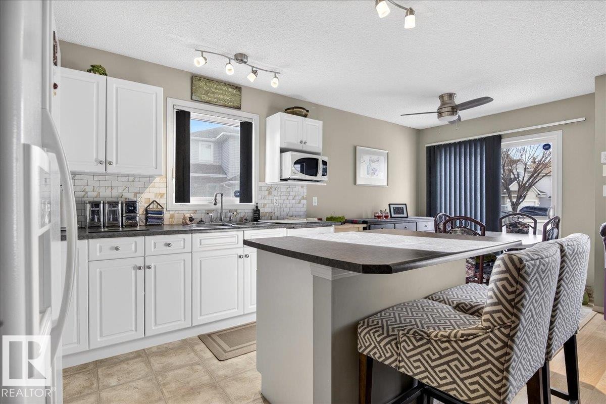 Kitchen with dark countertops, white appliances, a kitchen bar, decorative backsplash, and a center island - 23 4020 21 Street, Edmonton, AB - Indoor Photo Showing Kitchen