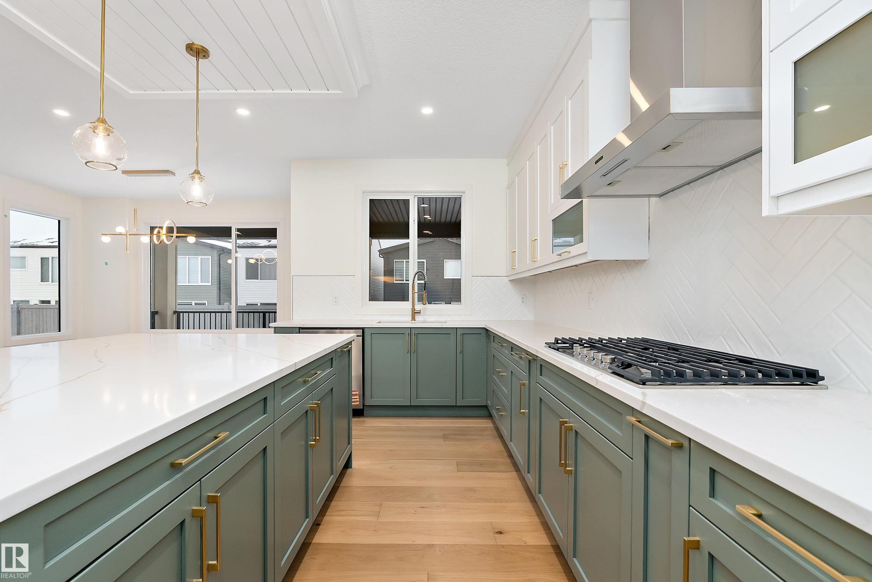 Kitchen with light wood finished floors, decorative light fixtures, two tone cabinetry, light stone countertops, and backsplash - Edmonton, AB - Indoor Photo Showing Kitchen With Upgraded Kitchen