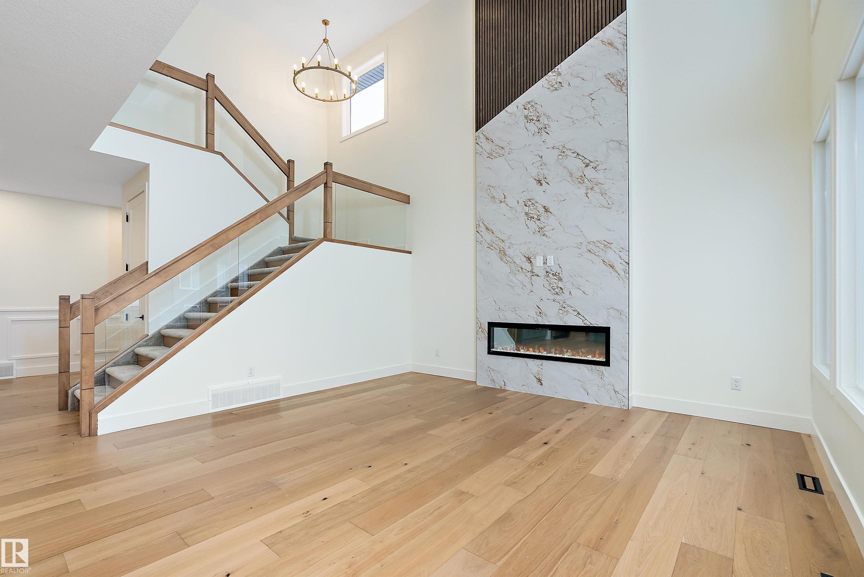 Unfurnished living room featuring a high ceiling, a high end fireplace, light wood-style flooring, and hanging lights - Edmonton, AB - Indoor Photo Showing Other Room With Fireplace