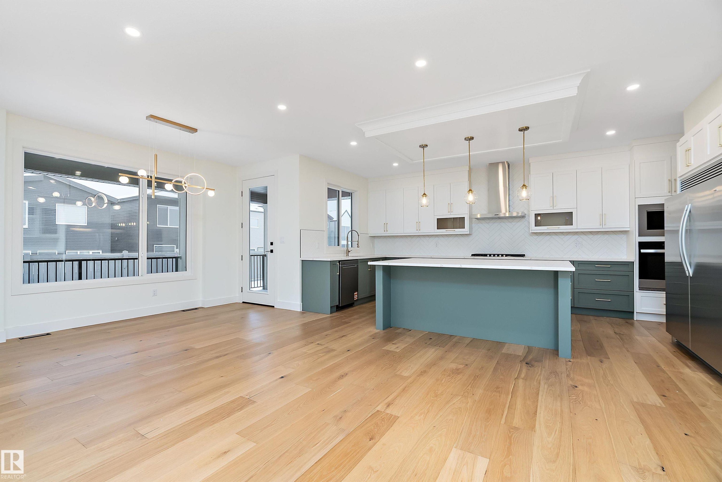 Kitchen with two tone color scheme, stainless steel appliances, a kitchen island, light wood finished floors, and decorative backsplash - Edmonton, AB - Indoor Photo Showing Kitchen With Upgraded Kitchen