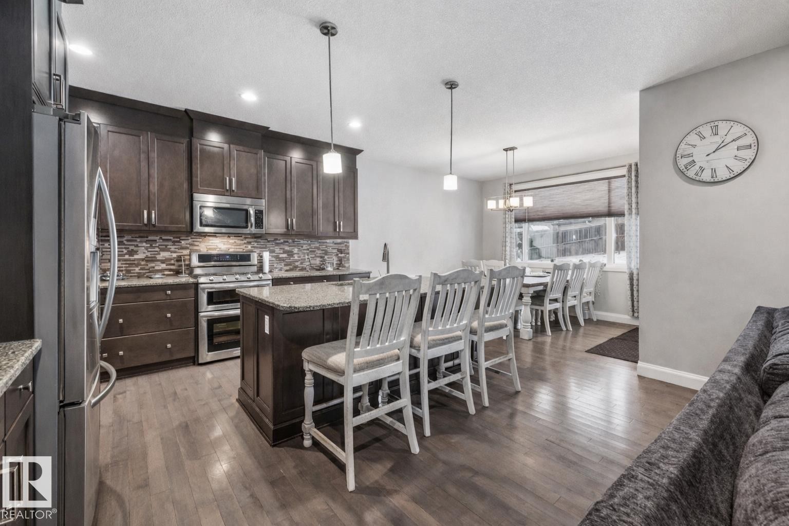 Kitchen with a kitchen bar, dark wood finish cabinets, stainless steel appliances, a center island, and hanging light fixtures - 14 Spring Bay, Spruce Grove, AB - Indoor
