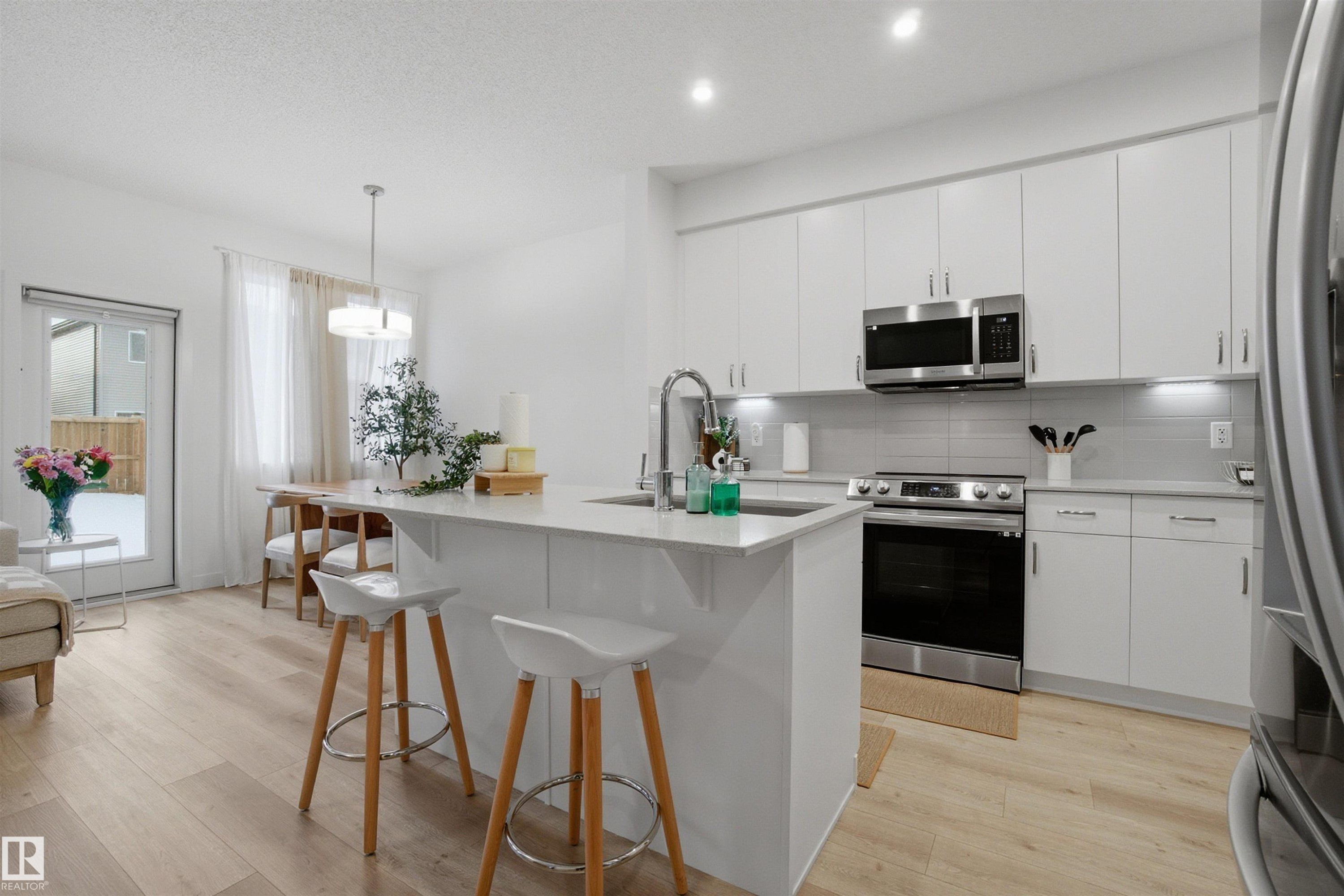 Kitchen featuring light wood-style flooring, stainless steel appliances, hanging light fixtures, and a center island with sink - 9882 225A St Nw, Edmonton, AB - Indoor Photo Showing Kitchen With Upgraded Kitchen