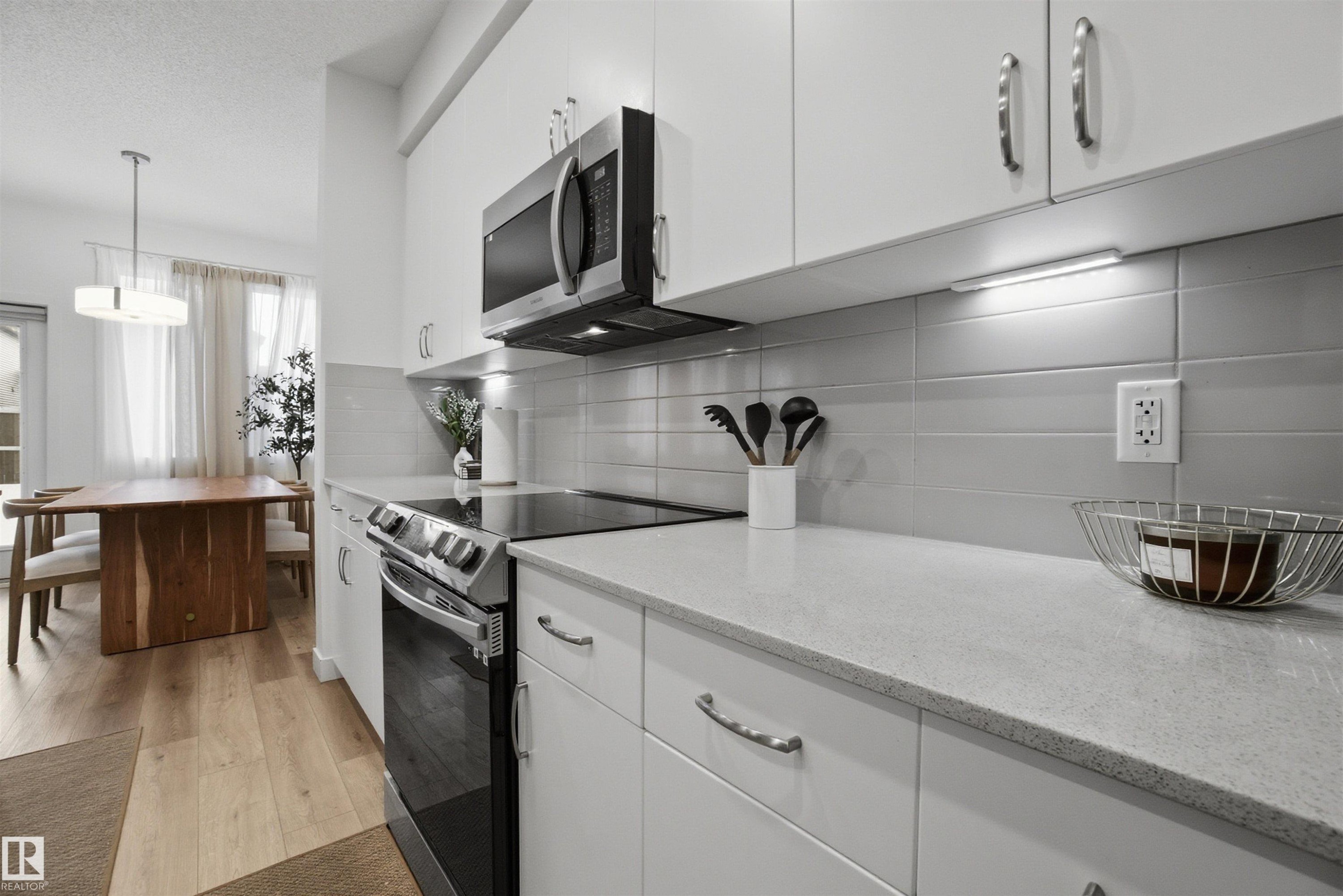 Kitchen with electric stove, white cabinetry, stainless steel microwave, tasteful backsplash, and light wood-style floors - 9882 225A St Nw, Edmonton, AB - Indoor Photo Showing Kitchen With Upgraded Kitchen