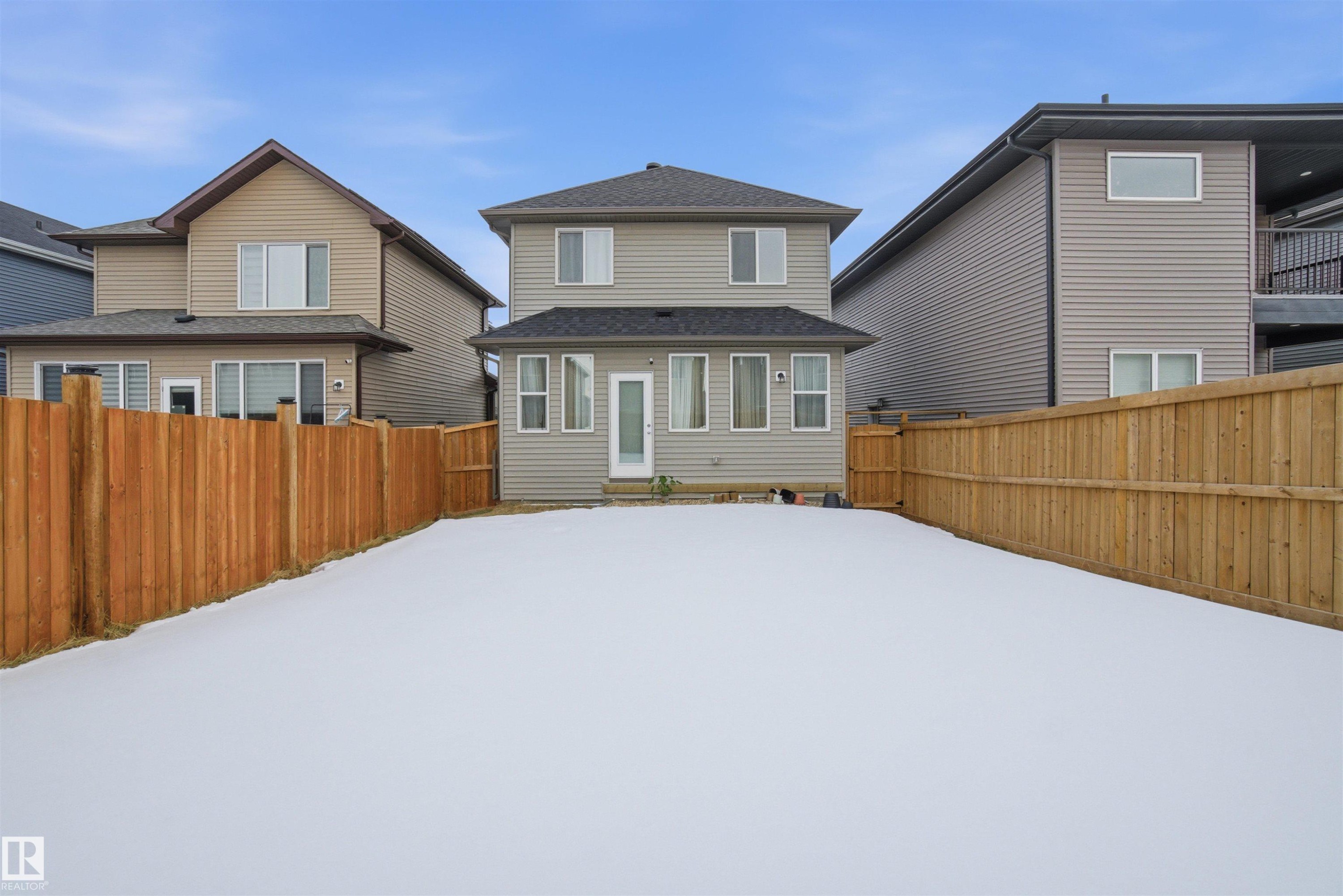 Snow covered rear of property featuring a fenced backyard and a shingled roof - 9882 225A St Nw, Edmonton, AB - Outdoor With Exterior