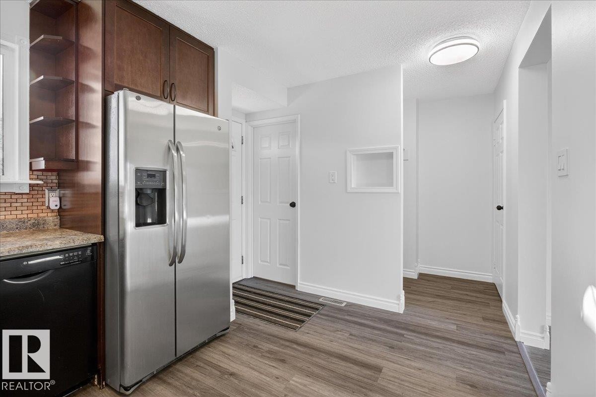 Kitchen featuring stainless steel fridge, black dishwasher, a textured ceiling, open shelves, and dark wood-style floors - 133 Habitat Crescent, Edmonton, AB - Indoor Photo Showing Other Room