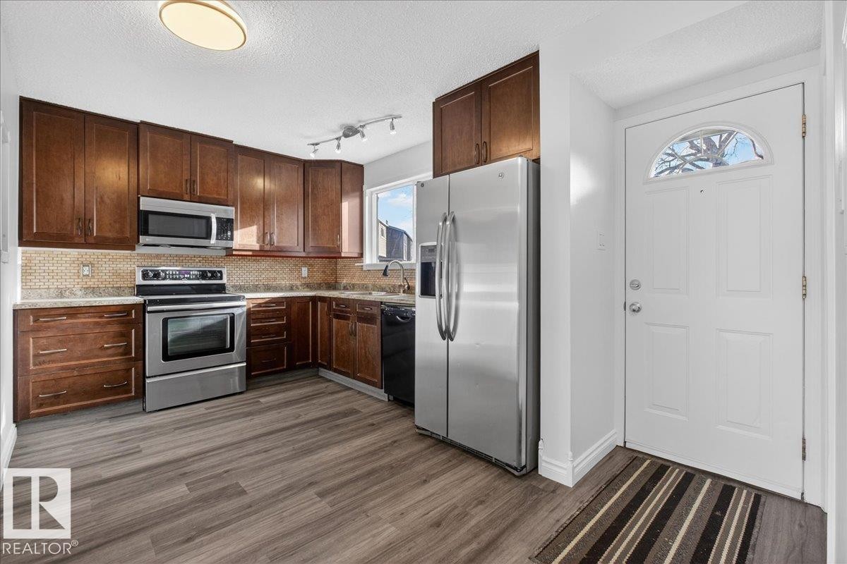 Kitchen featuring stainless steel appliances, a textured ceiling, dark wood finish cabinets, decorative backsplash, and dark wood-type flooring - 133 Habitat Crescent, Edmonton, AB - Indoor Photo Showing Kitchen With Stainless Steel Kitchen