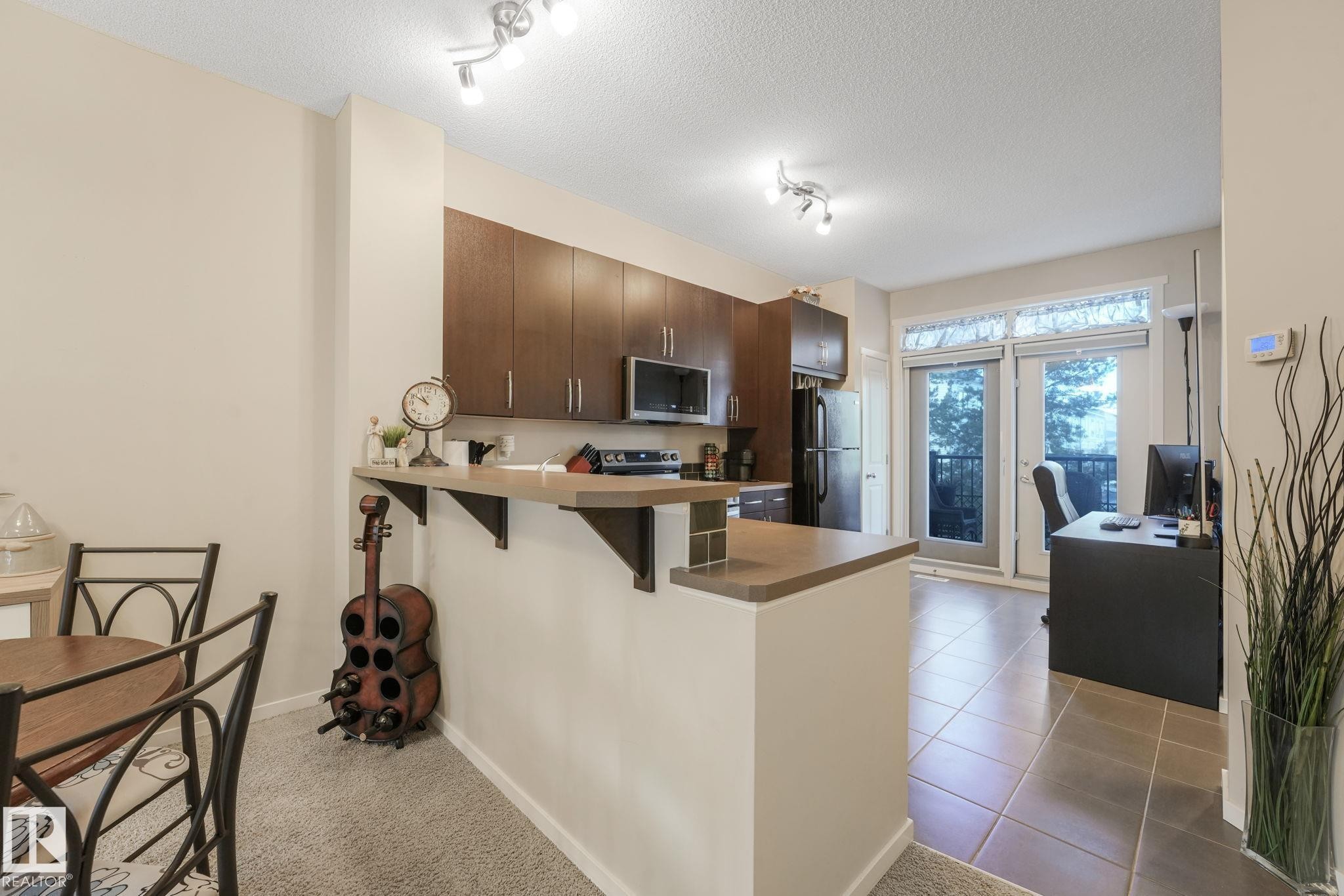 Kitchen featuring a peninsula, dark wood finish cabinets, a kitchen breakfast bar, stainless steel appliances, and a textured ceiling - 91 603 Watt Boulevard, Edmonton, AB - Indoor Photo Showing Kitchen