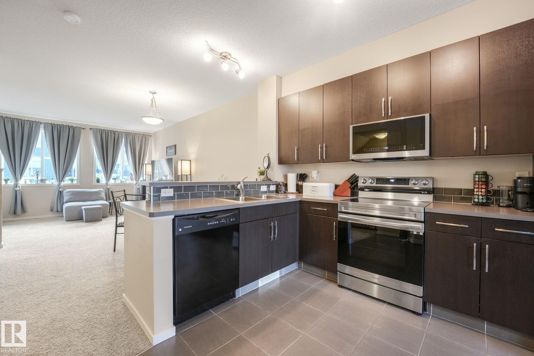 Kitchen with stainless steel appliances, open floor plan, dark wood finish cabinetry, a peninsula, and light carpet - 91 603 Watt Boulevard, Edmonton, AB - Indoor Photo Showing Kitchen With Double Sink