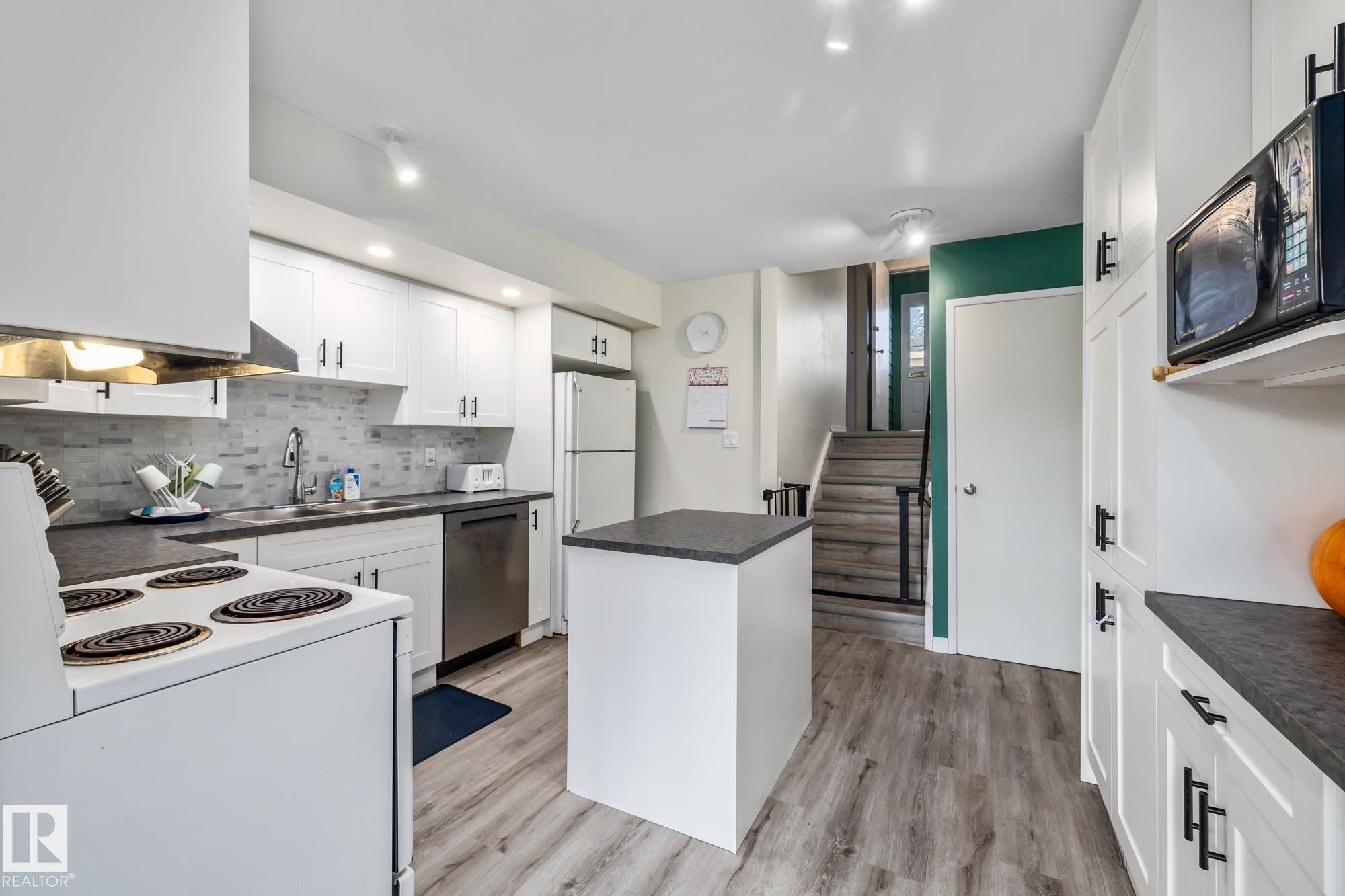 Kitchen with white appliances, dark countertops, a kitchen island, and white cabinetry - 11 Grandview Ridge, St. Albert, AB - Indoor Photo Showing Kitchen