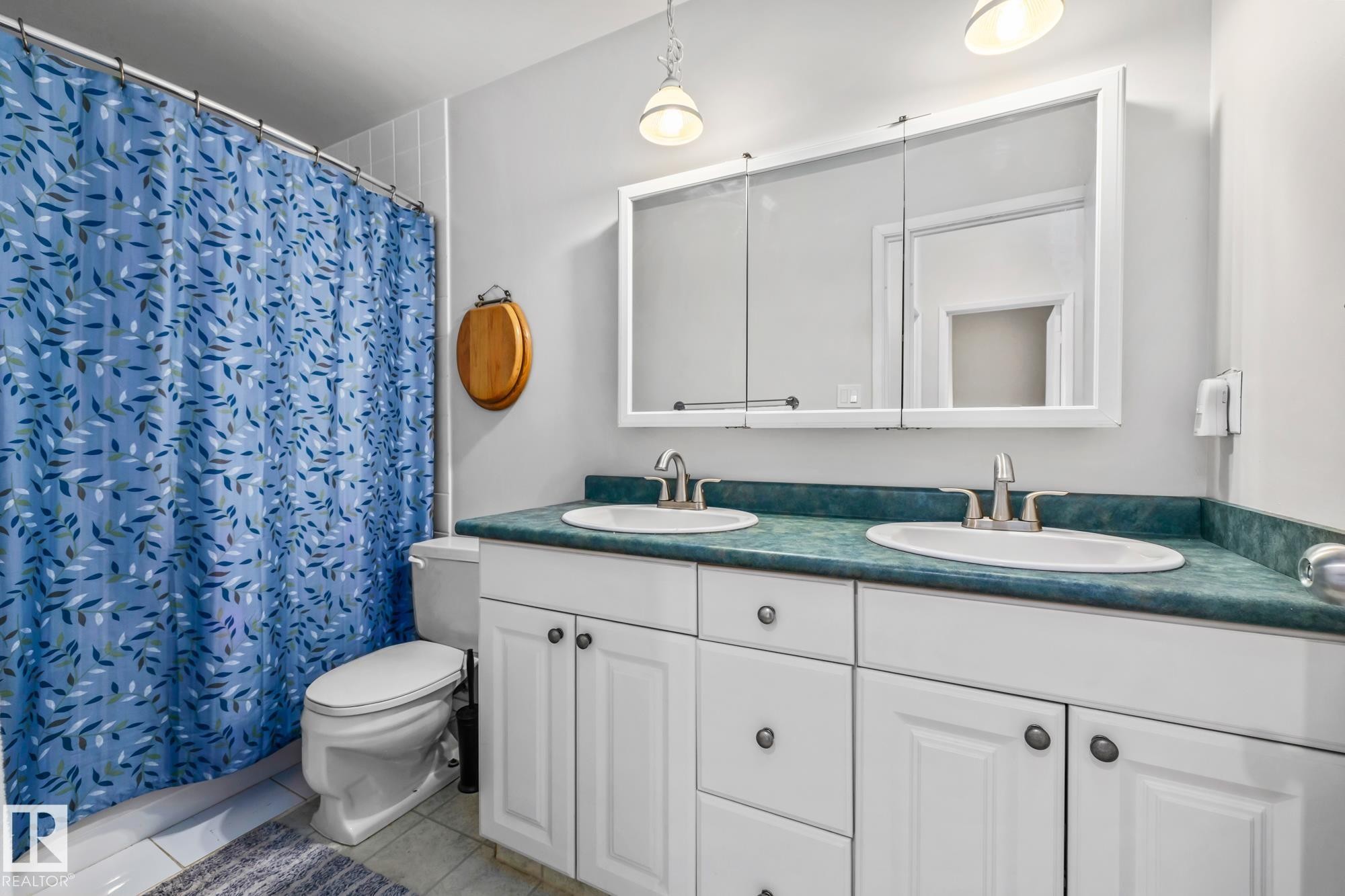 Bathroom featuring a shower with curtain, double vanity, and light tile patterned floors - 11 Grandview Ridge, St. Albert, AB - Indoor Photo Showing Bathroom