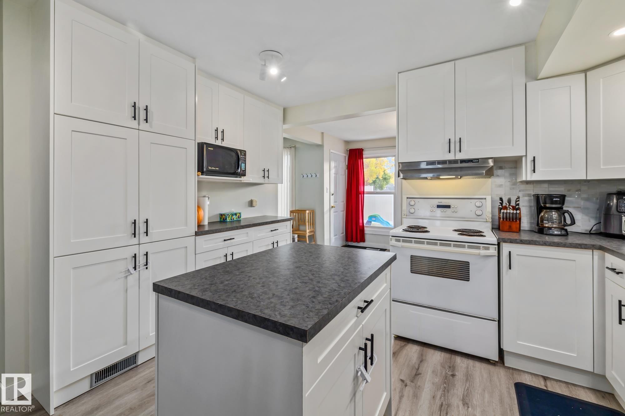 Kitchen featuring white electric range, white cabinets, dark countertops, light wood finished floors, and black microwave - 11 Grandview Ridge, St. Albert, AB - Indoor Photo Showing Kitchen