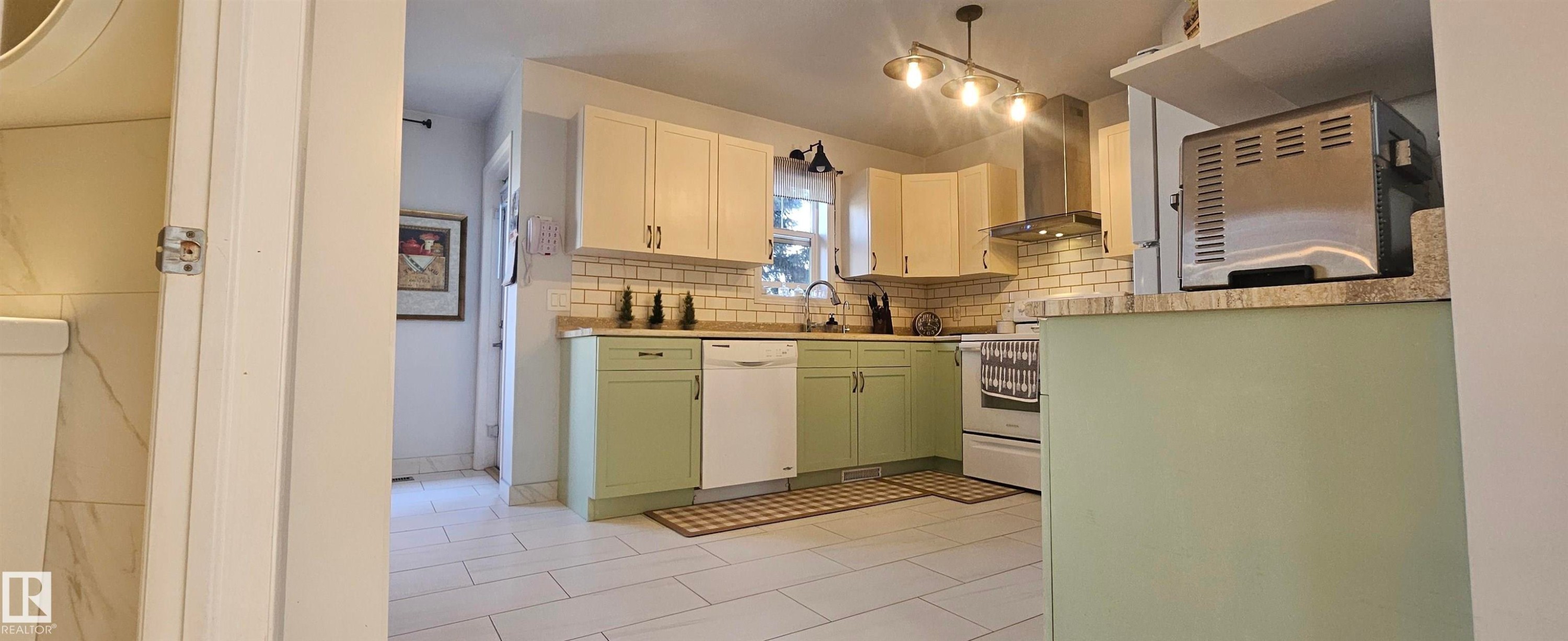 Two tone kitchen featuring two tone cabinets, backsplash, white appliances, light countertops, and light tile patterned floors - 208 178 Bridgeport Boulevard, Leduc, AB - Indoor Photo Showing Kitchen