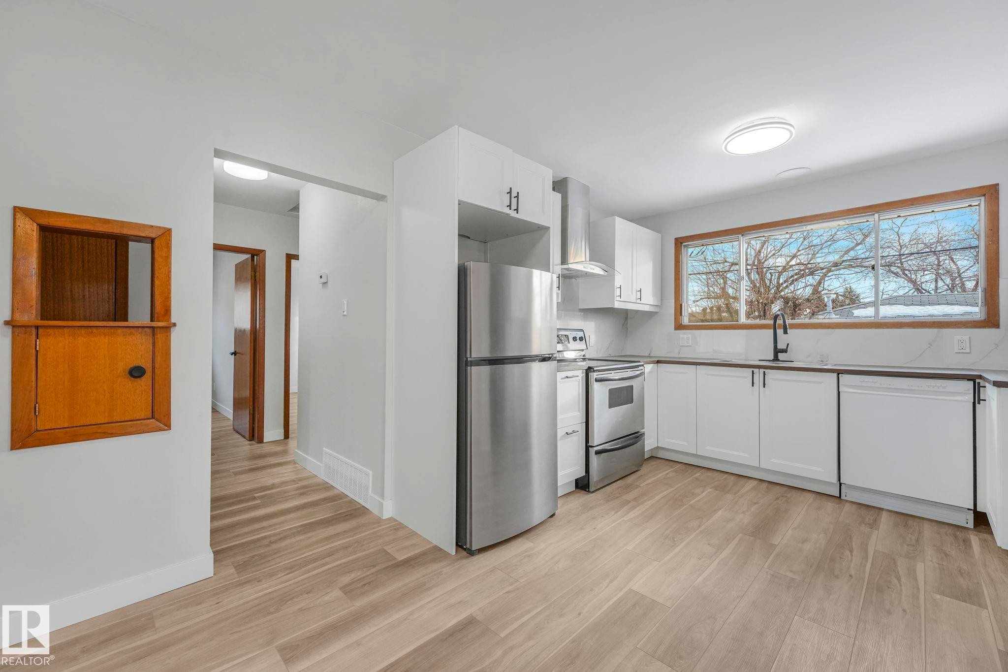 Kitchen with stainless steel appliances, white cabinetry, and light wood-style flooring - 6007 95 Avenue, Edmonton, AB - Indoor Photo Showing Kitchen