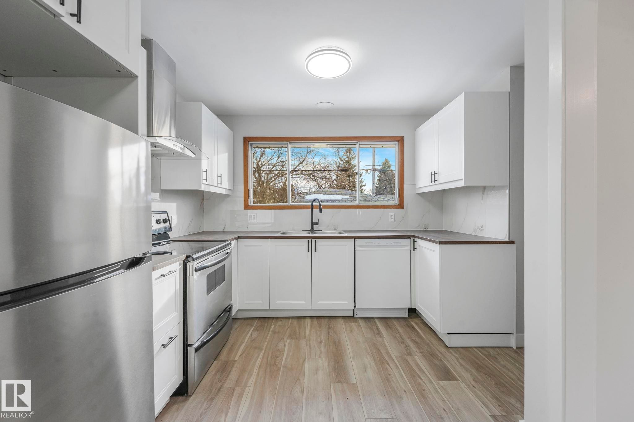 Kitchen with stainless steel appliances, light wood-type flooring, and white cabinetry - 6007 95 Avenue, Edmonton, AB - Indoor Photo Showing Kitchen With Double Sink
