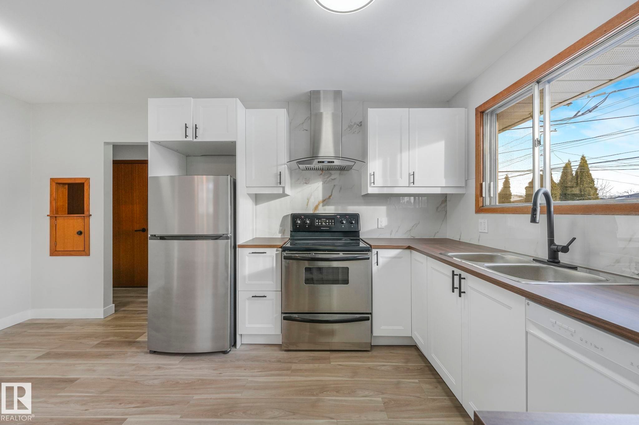 Kitchen with stainless steel appliances, white cabinets, and light wood-type flooring - 6007 95 Avenue, Edmonton, AB - Indoor Photo Showing Kitchen With Double Sink