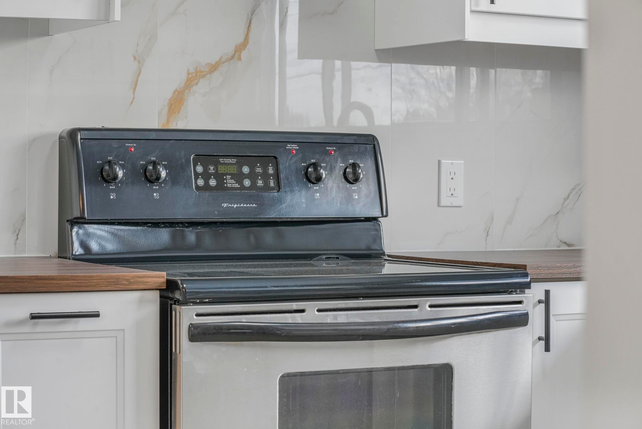 Kitchen view of electric range oven, white cabinets, and wood counters - 6007 95 Avenue, Edmonton, AB - Indoor Photo Showing Kitchen