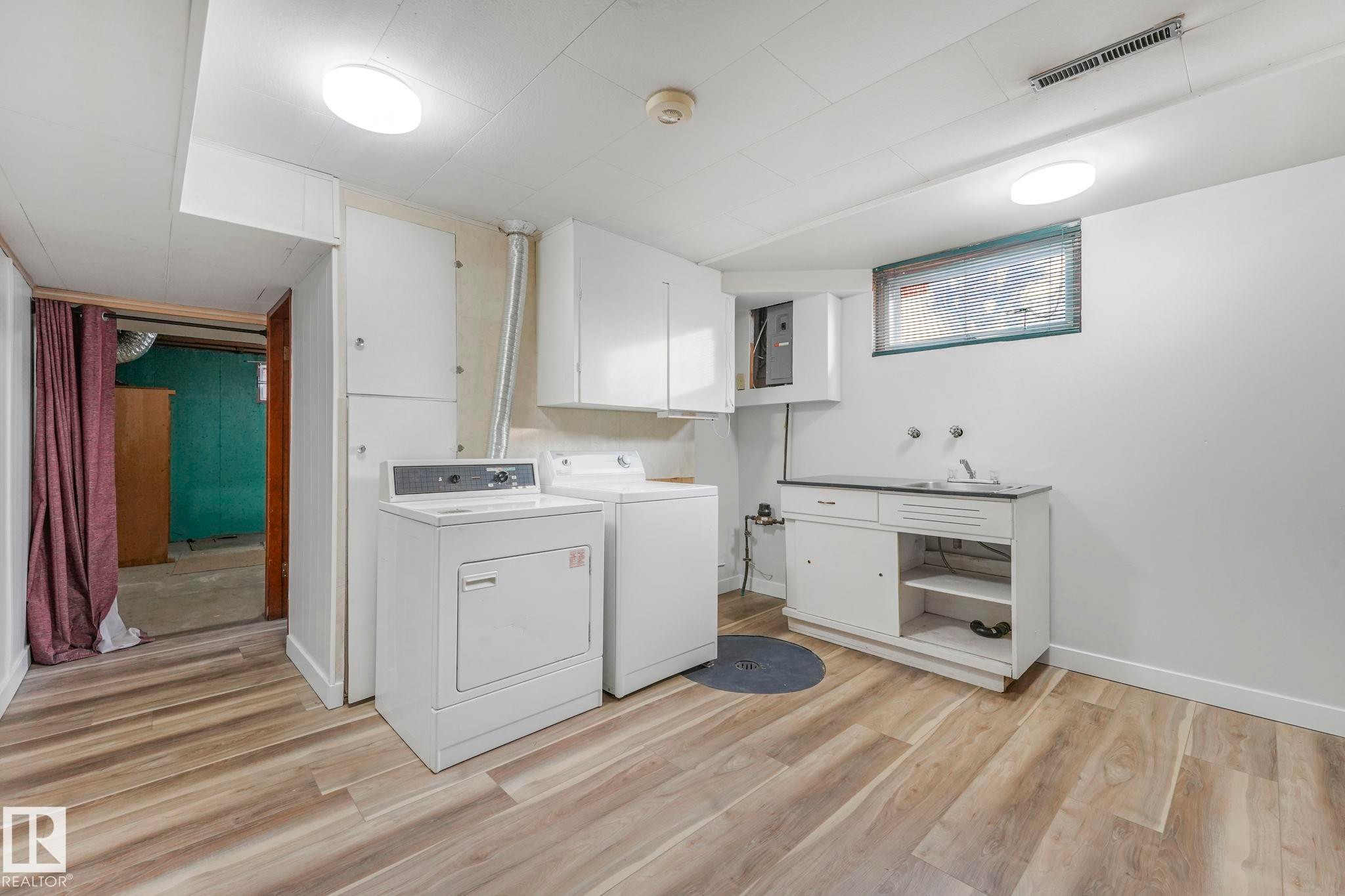 Laundry area featuring light wood-style flooring, washer and dryer, and electric panel - 6007 95 Avenue, Edmonton, AB - Indoor Photo Showing Laundry Room