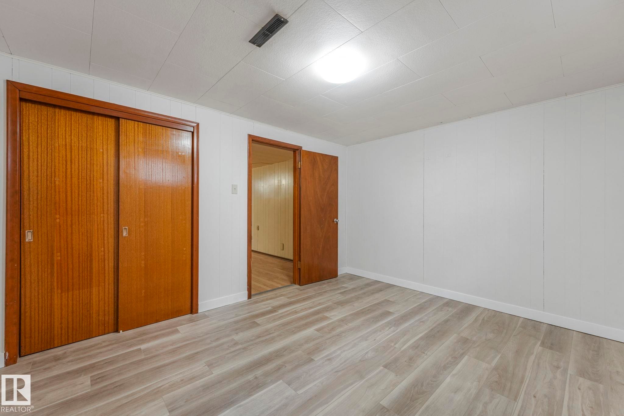 Unfurnished bedroom with a closet, light wood-style floors, and wood walls - 6007 95 Avenue, Edmonton, AB - Indoor Photo Showing Other Room
