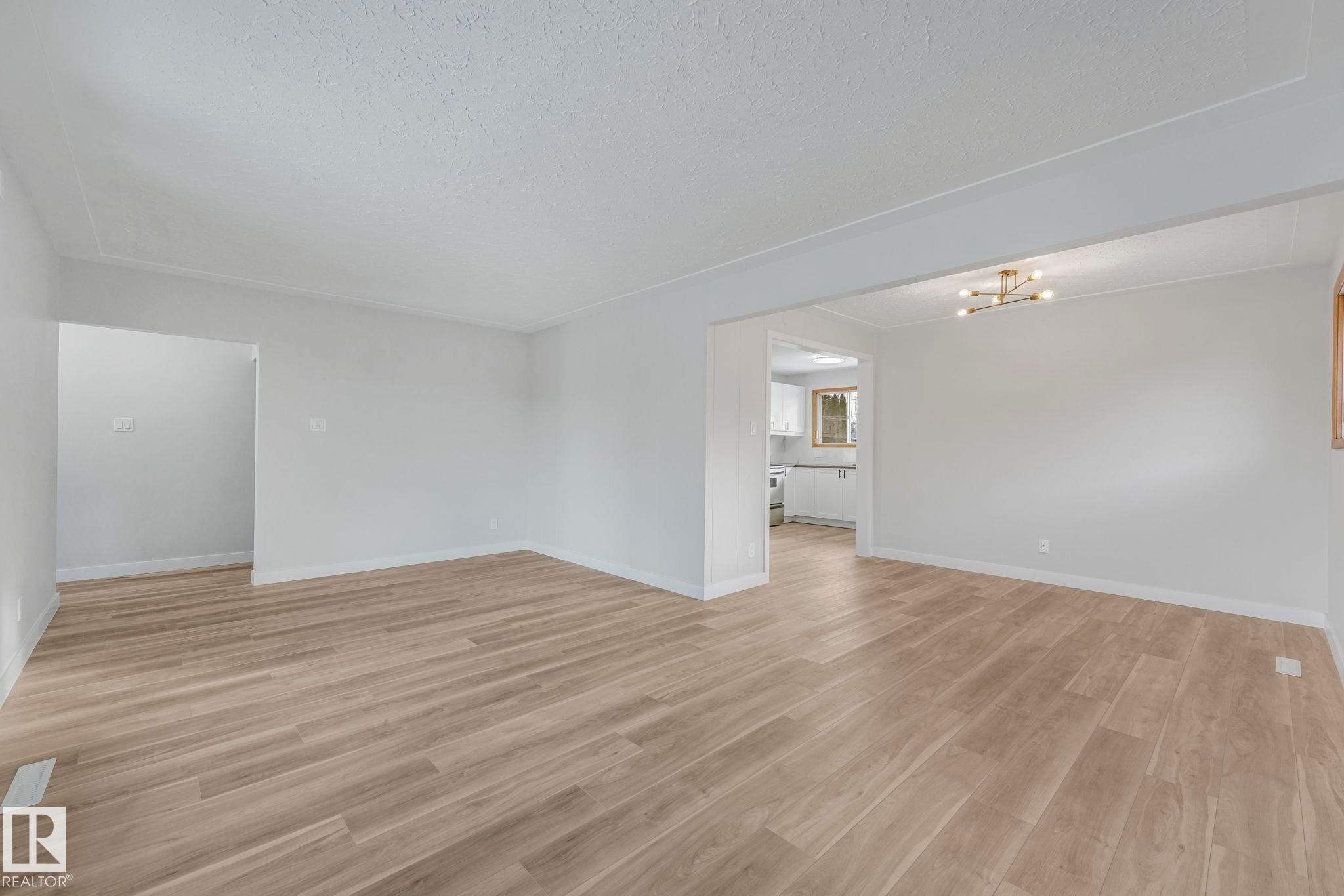 Unfurnished room featuring light wood-style floors, a textured ceiling, and hanging lights - 6007 95 Avenue, Edmonton, AB - Indoor Photo Showing Other Room