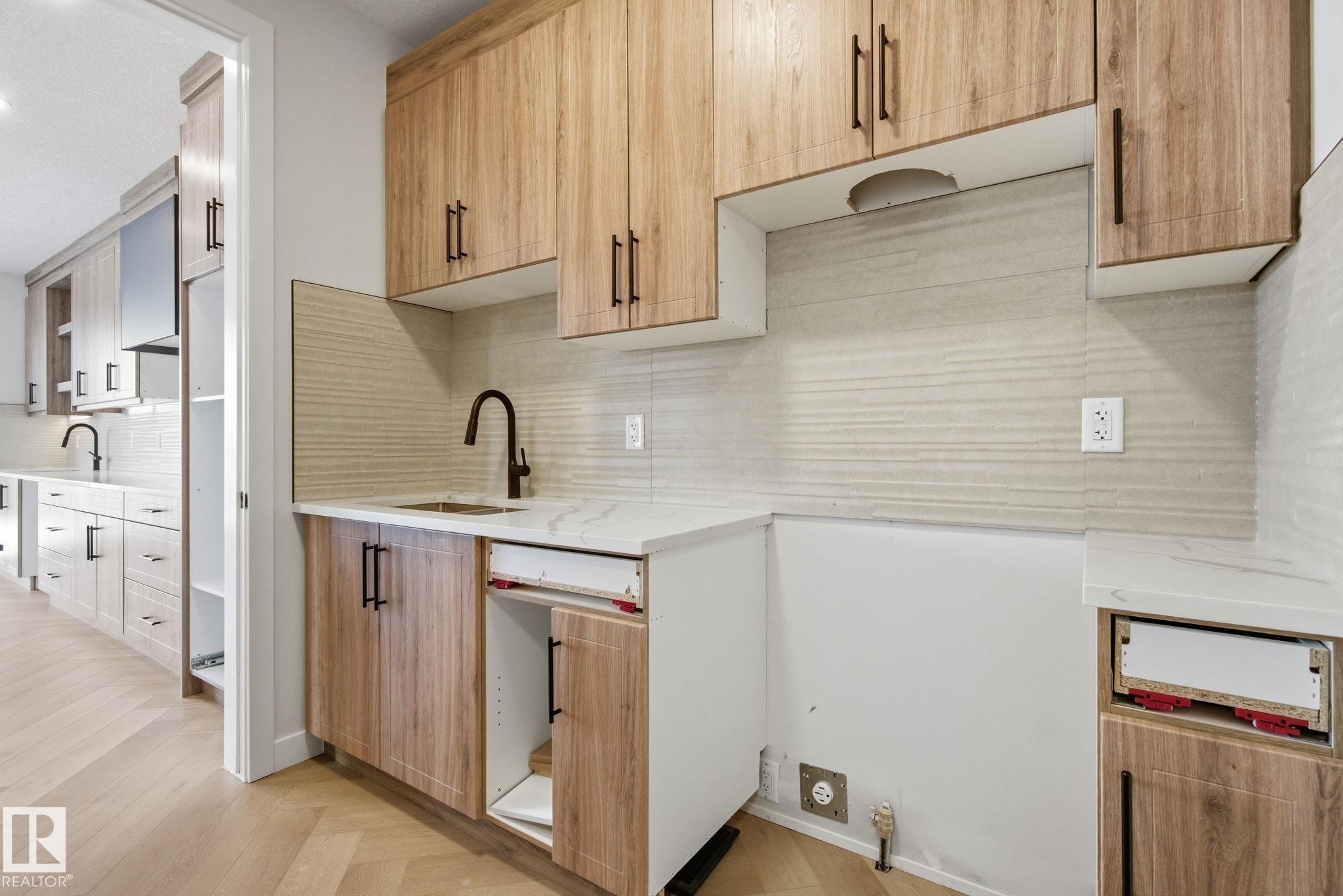Two tone kitchen featuring parquet flooring, decorative backsplash, light stone countertops, and dual tone cabinetry - 17108 2 Street, Edmonton, AB - Indoor Photo Showing Kitchen