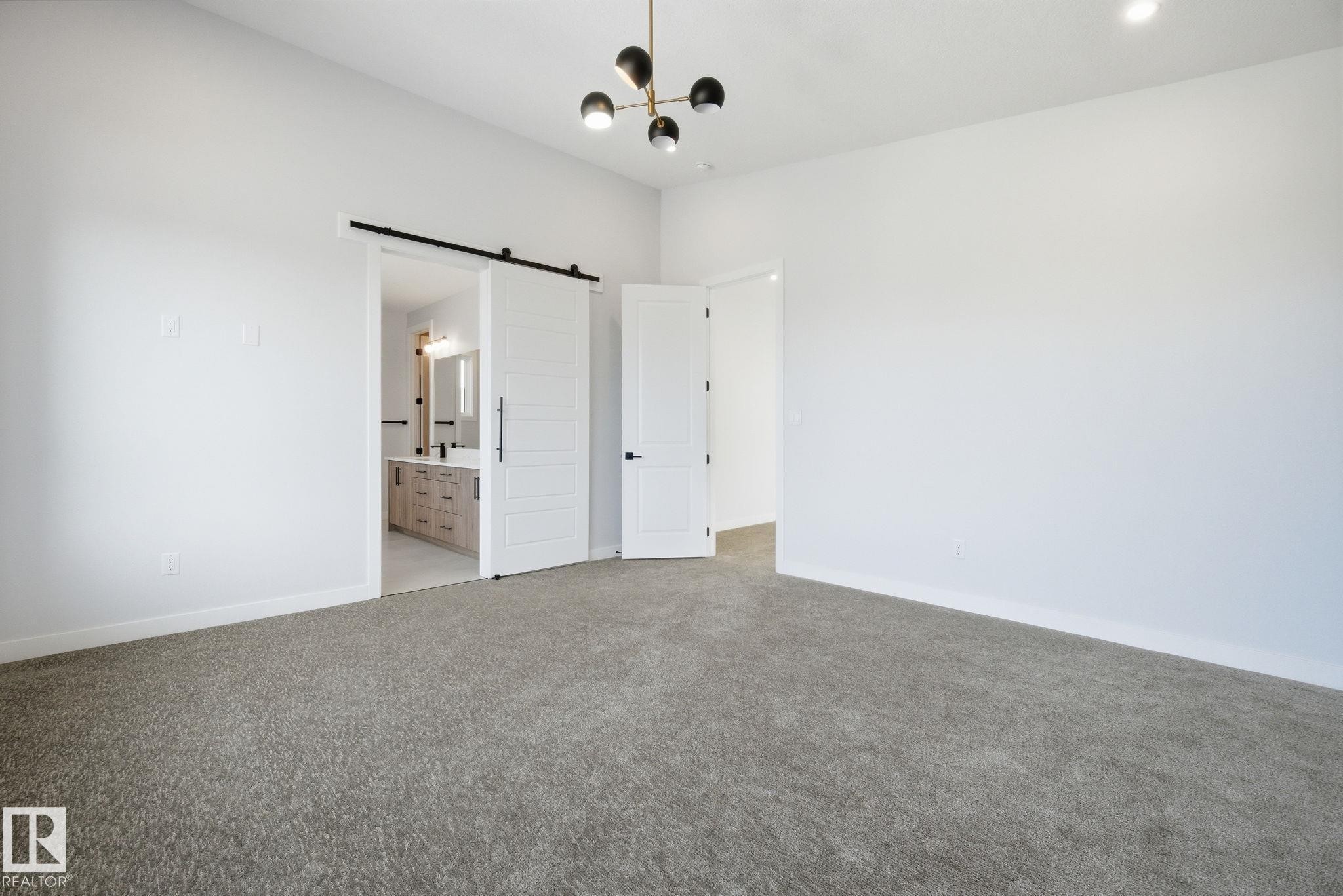 Unfurnished bedroom featuring a barn door, light carpet, ensuite bath, and suspended lighting - 17108 2 Street, Edmonton, AB - Indoor Photo Showing Other Room