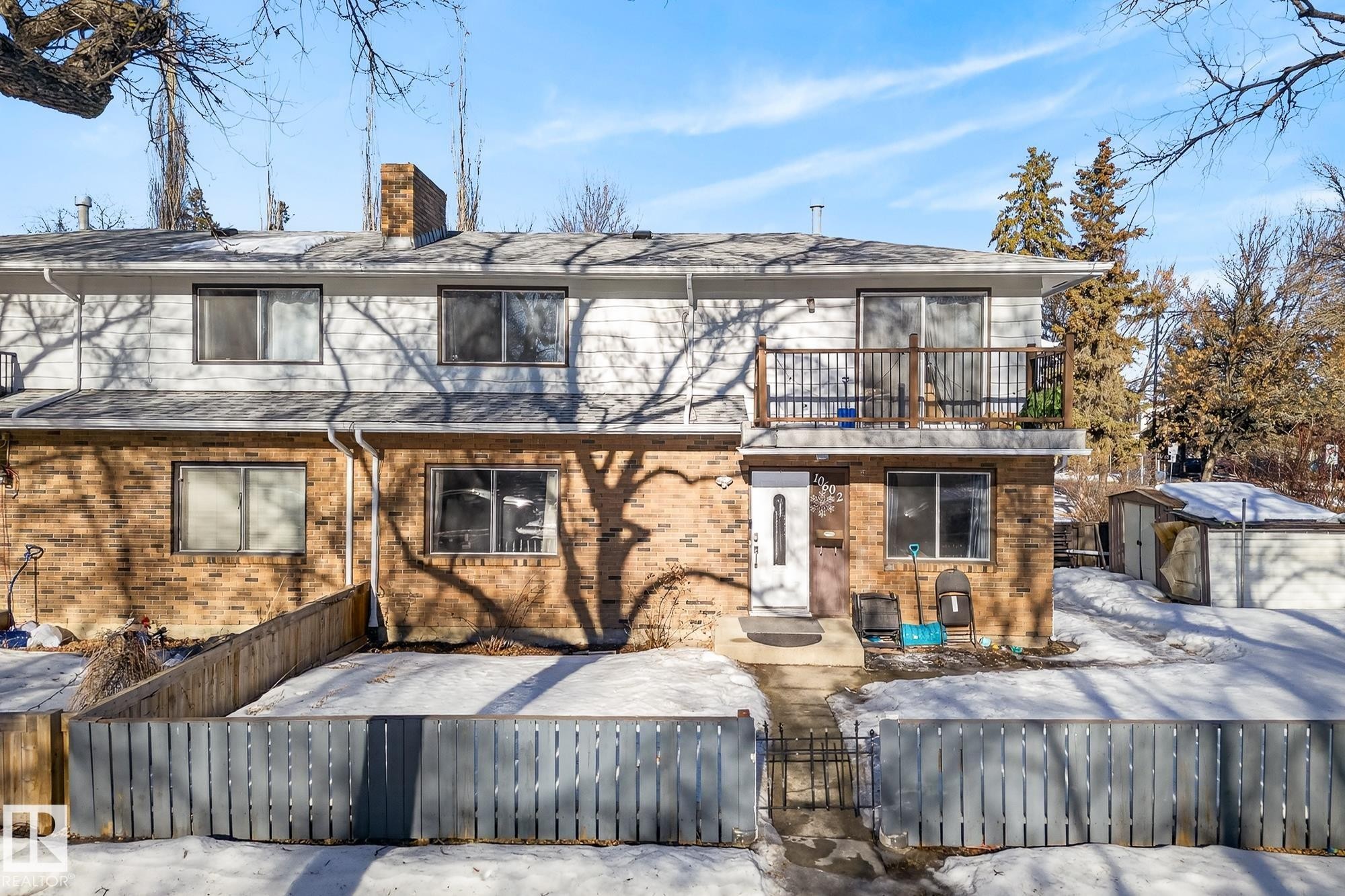 Snow covered back of property with an outbuilding, a balcony, a fenced front yard, brick siding, and a gate - 10602 66 Avenue, Edmonton, AB - Outdoor