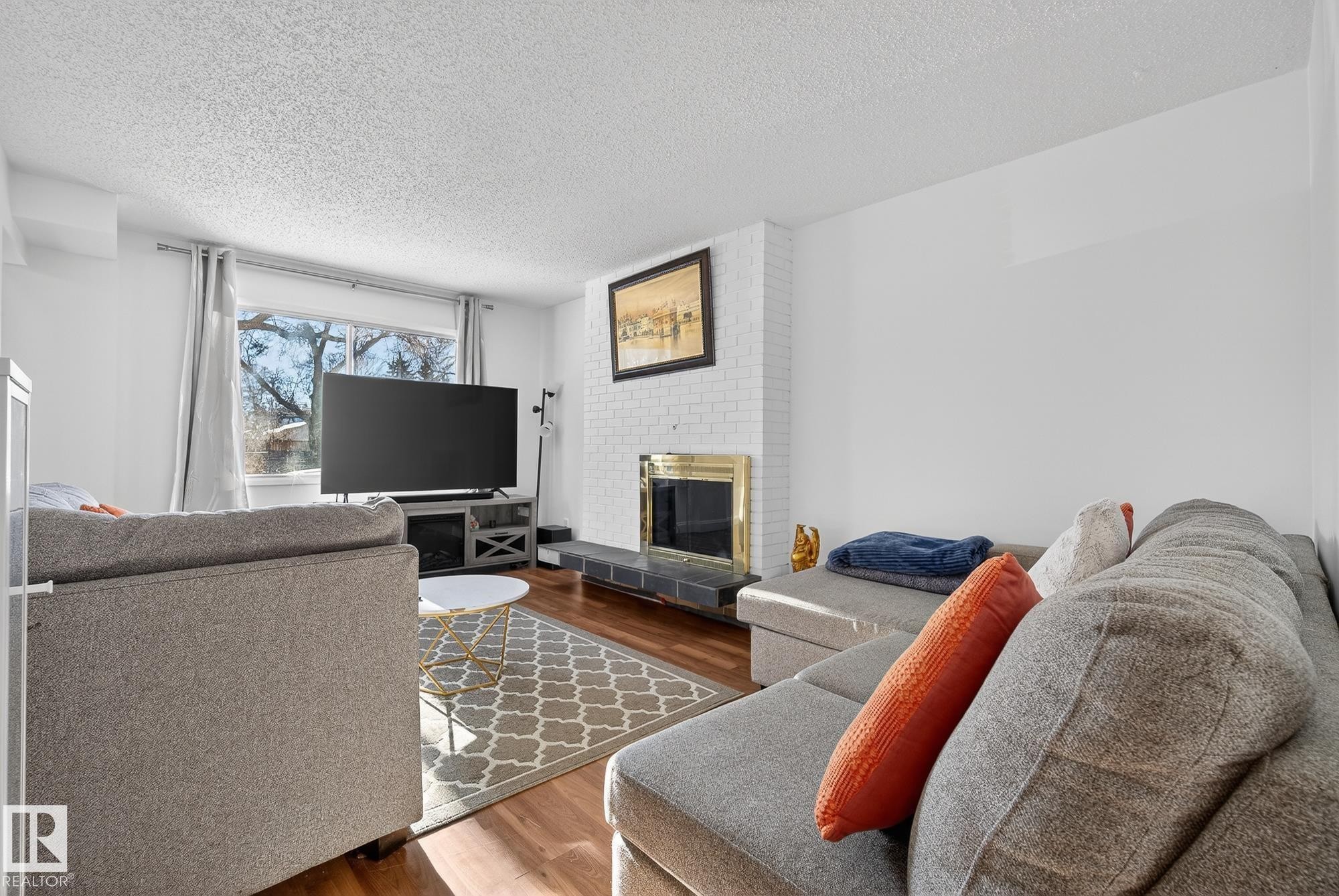 Living room with wood finished floors, a brick fireplace, and a textured ceiling - 10602 66 Avenue, Edmonton, AB - Indoor Photo Showing Living Room With Fireplace