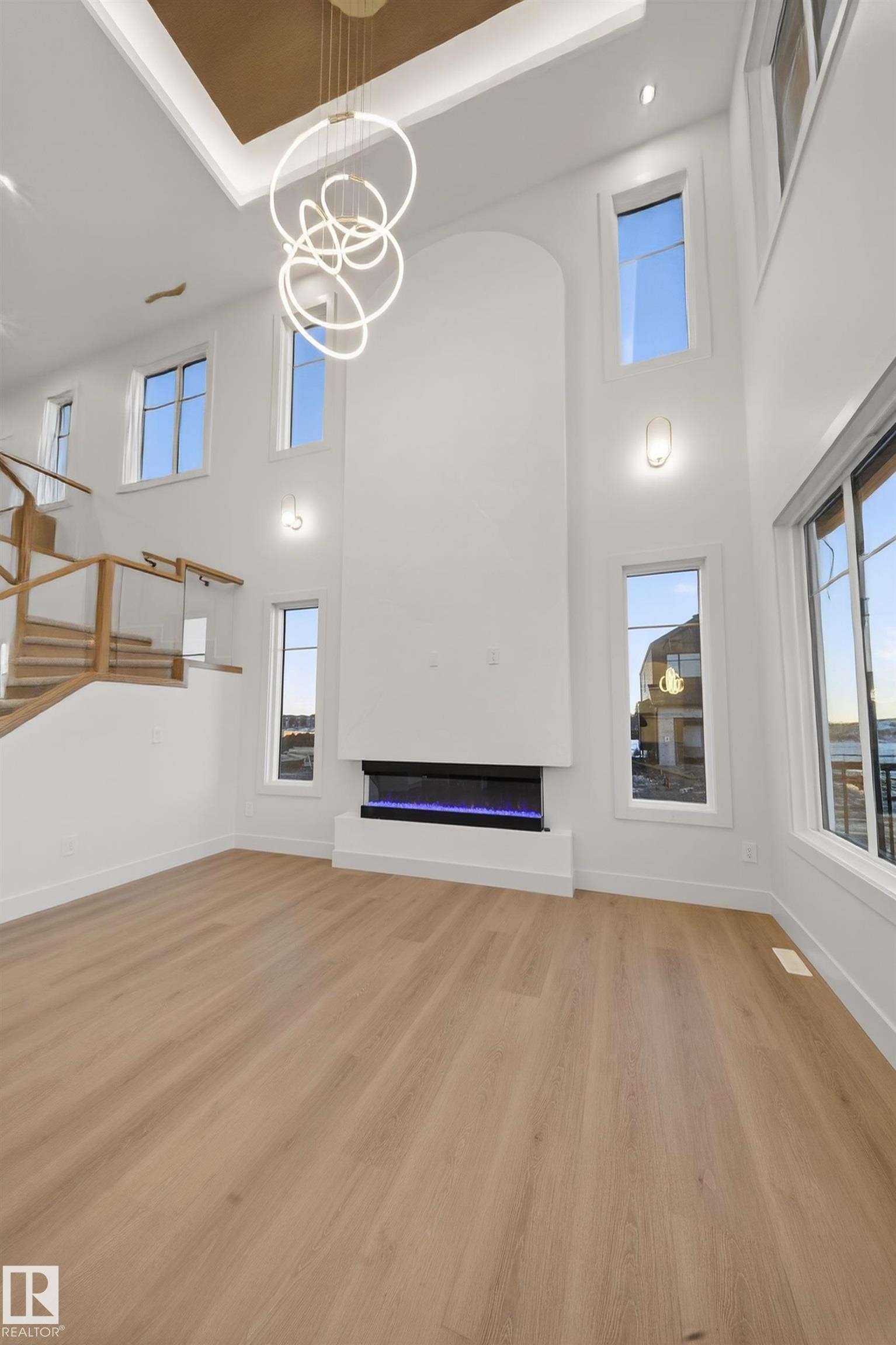 Unfurnished living room featuring a tray ceiling, light wood-type flooring, suspended lighting, and a glass covered fireplace - 8924 Mayday Way, Edmonton, AB