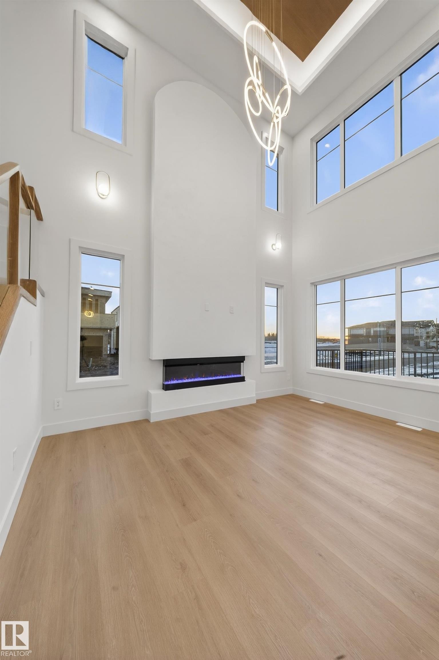 Unfurnished living room featuring light wood-style flooring, a high ceiling, a chandelier, a glass covered fireplace, and plenty of natural light - 8924 Mayday Way, Edmonton, AB