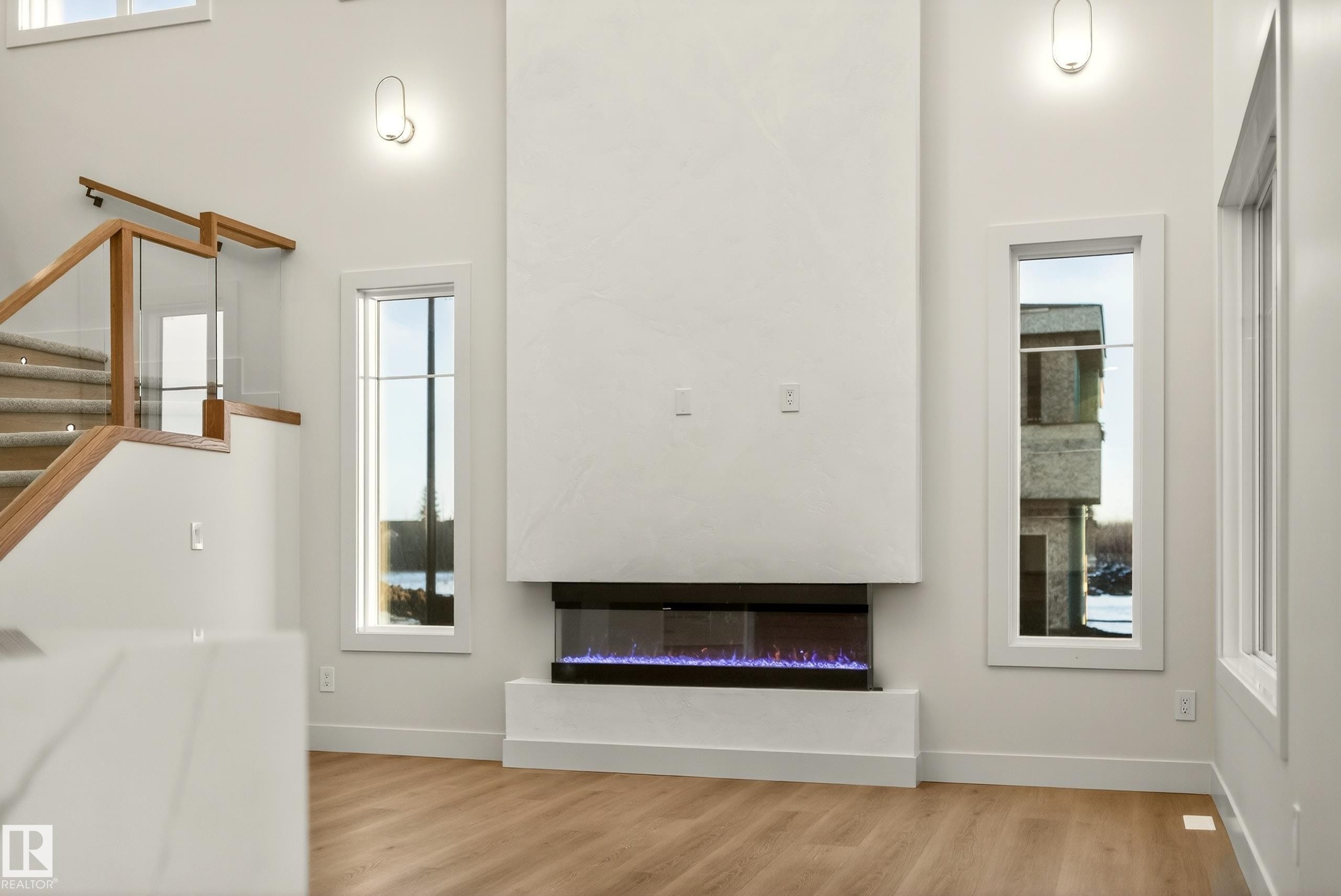 Unfurnished living room with a glass covered fireplace, wood finished floors, and a high ceiling - 8924 Mayday Way, Edmonton, AB