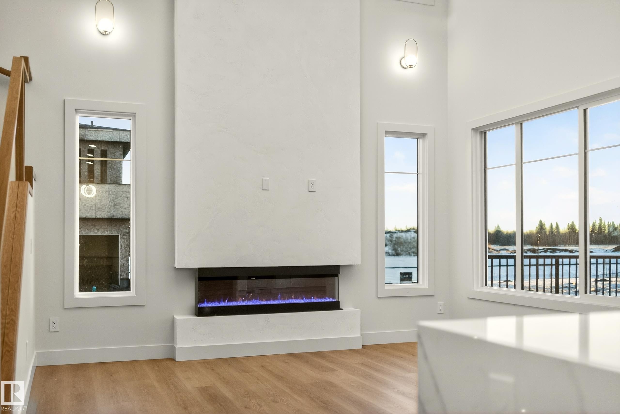 Unfurnished living room with a glass covered fireplace, light wood finished floors, a high ceiling, and a water view - 8924 Mayday Way, Edmonton, AB